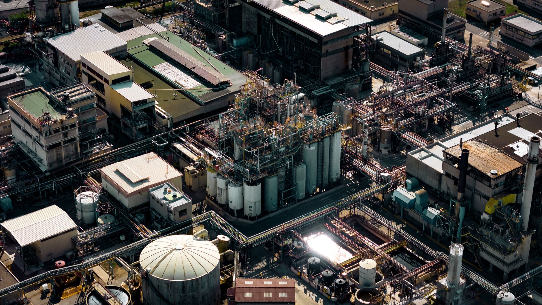 aerial view of an Iranian oil refinery complex with idle processing units and empty storage tanks under a hazy sky