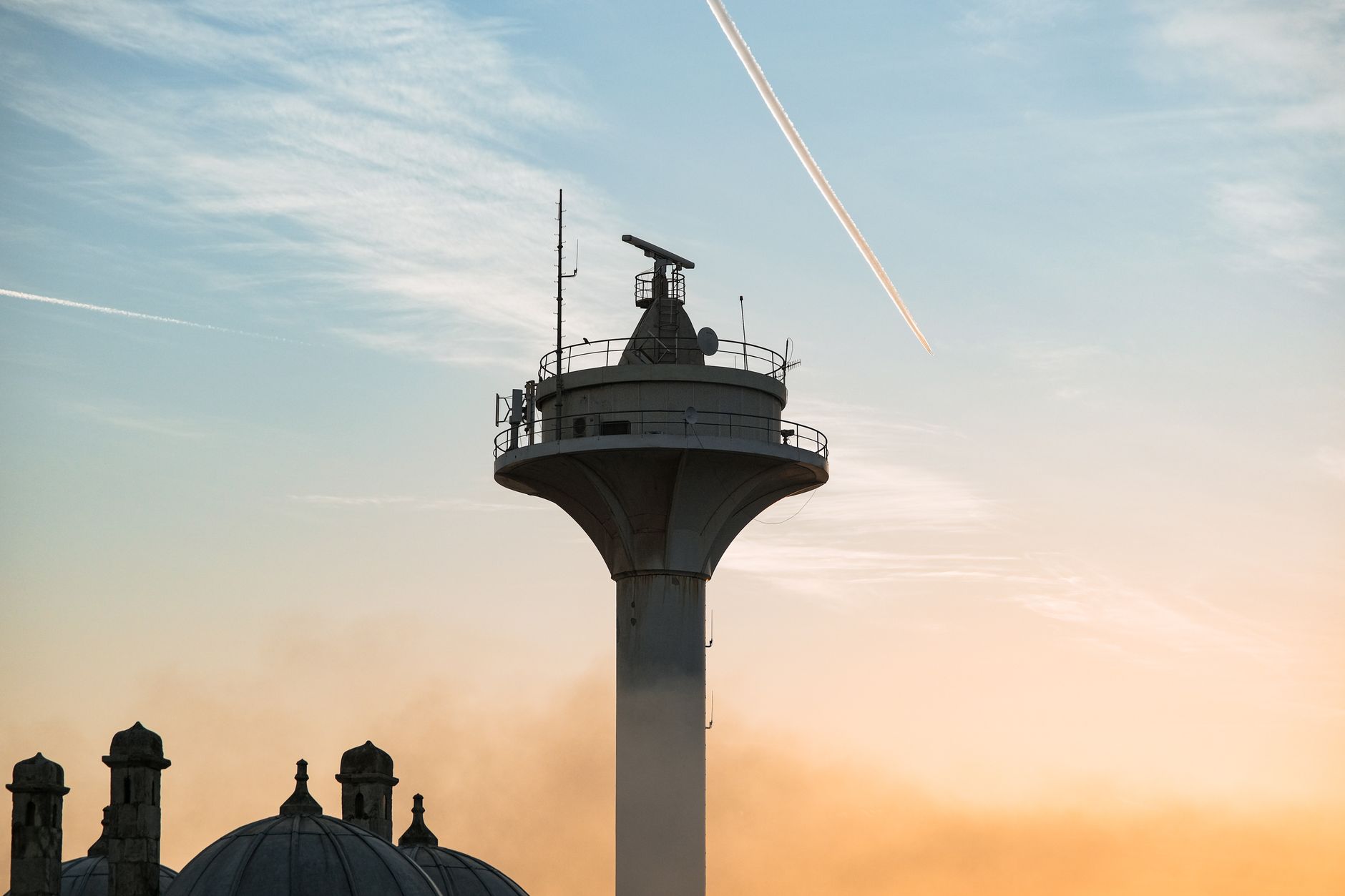 exterior of a modern military radar installation mounted on elevated ground, overlooking a Mediterranean coastal landscape at dusk