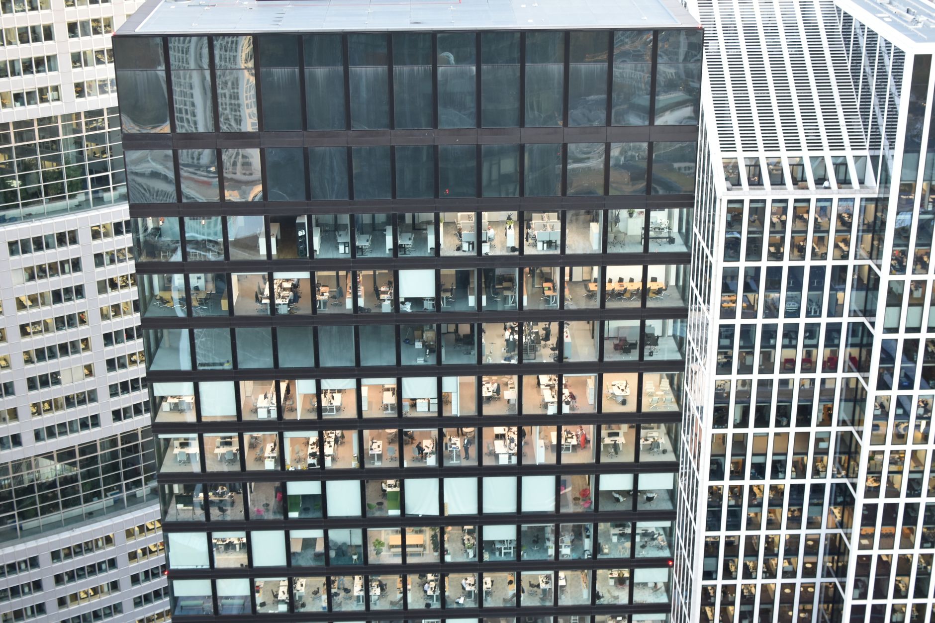 aerial view of a dense cluster of glass-fronted office towers in a modern business district, taken at dusk with interior lights visible through the facades
