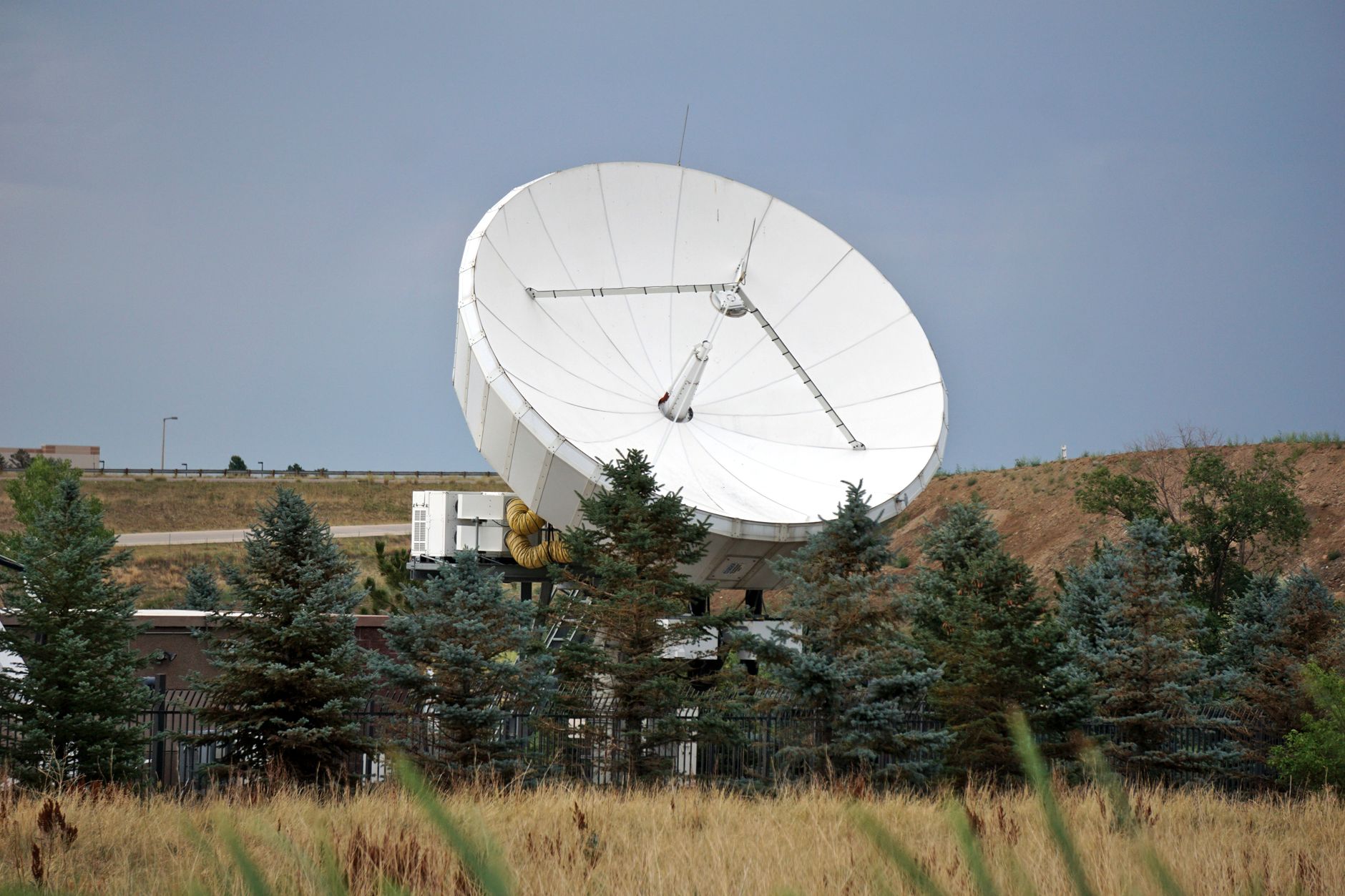 Aerial view of a satellite ground station antenna array in an arid landscape, large white dish receivers pointing skyward under a clear blue sky