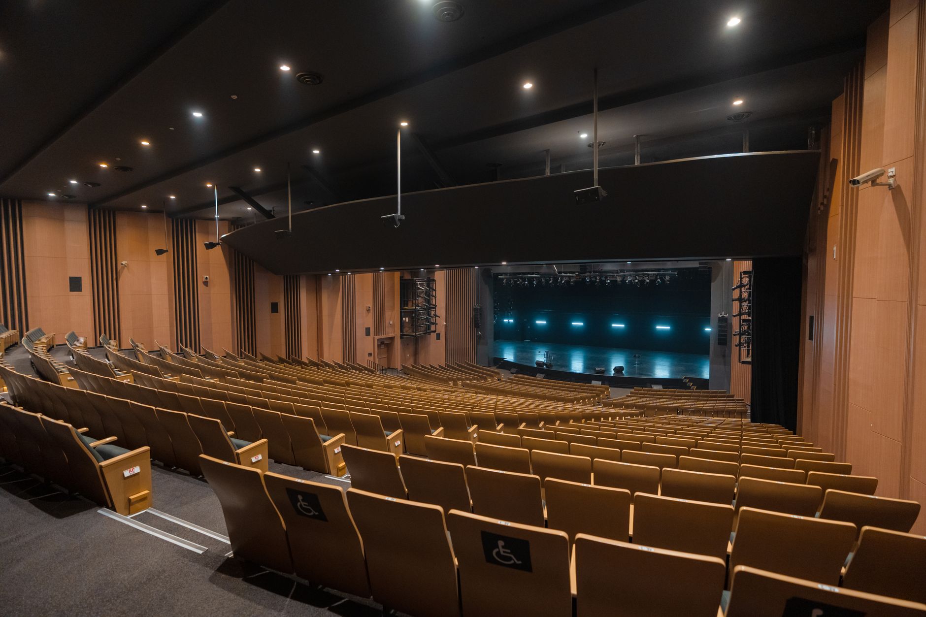 interior of a large conference hall with a curved stage lit by blue and white spotlights, a large screen displaying abstract circuit patterns in the background