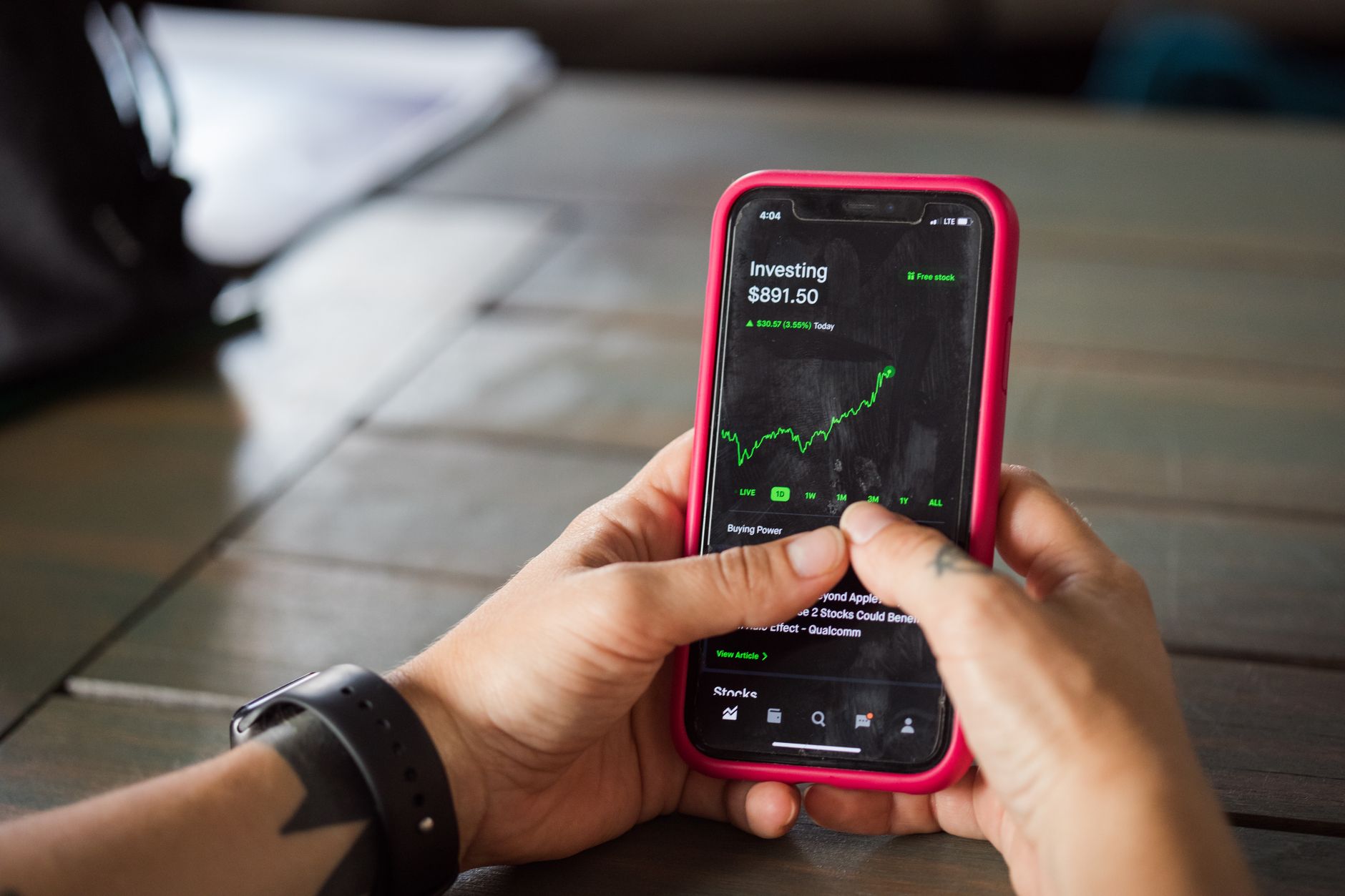 a smartphone resting on a wooden desk displaying a financial markets application interface with price charts visible on screen