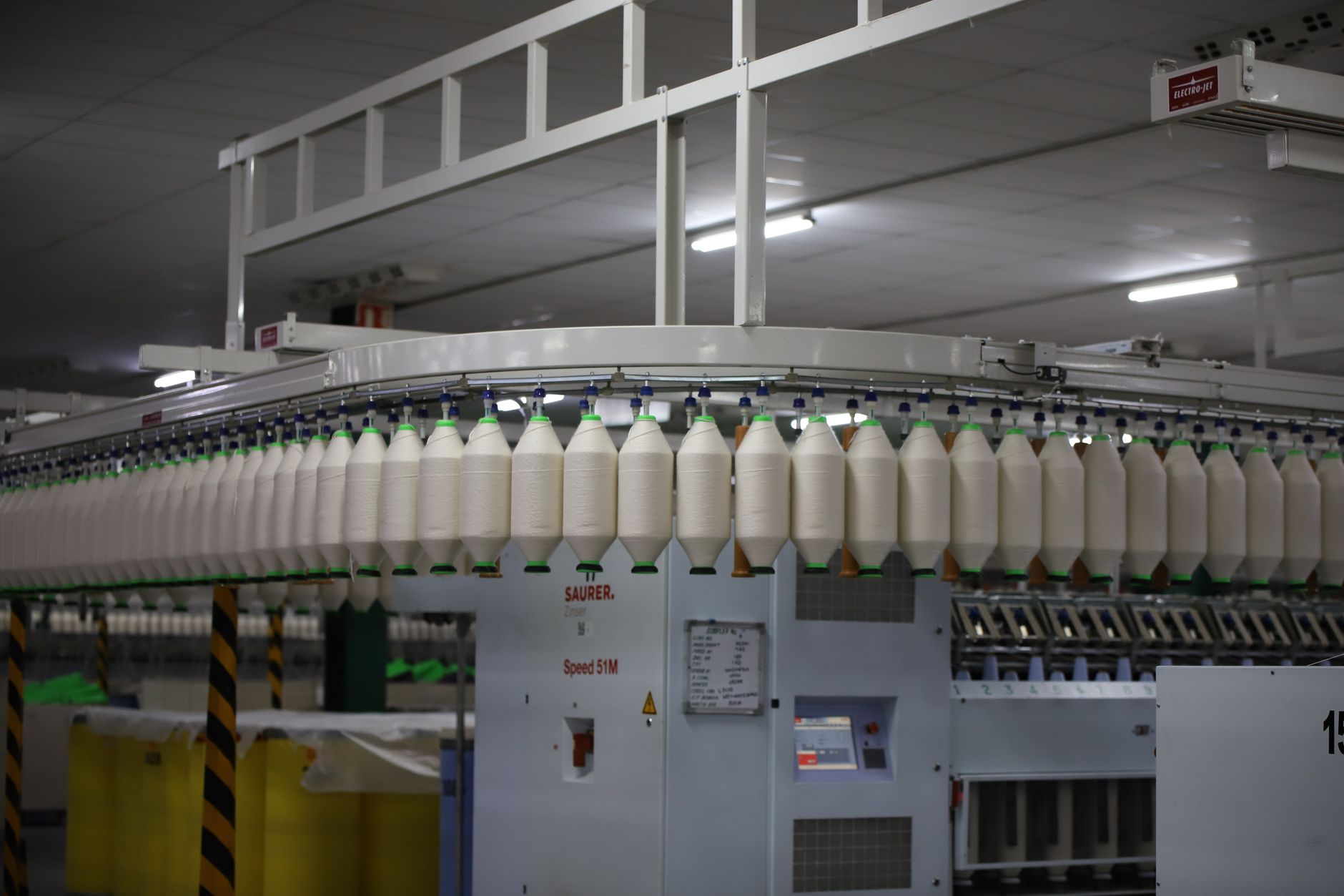 interior of an optical fiber manufacturing facility with spools of cable and precision machinery lit by overhead industrial lighting