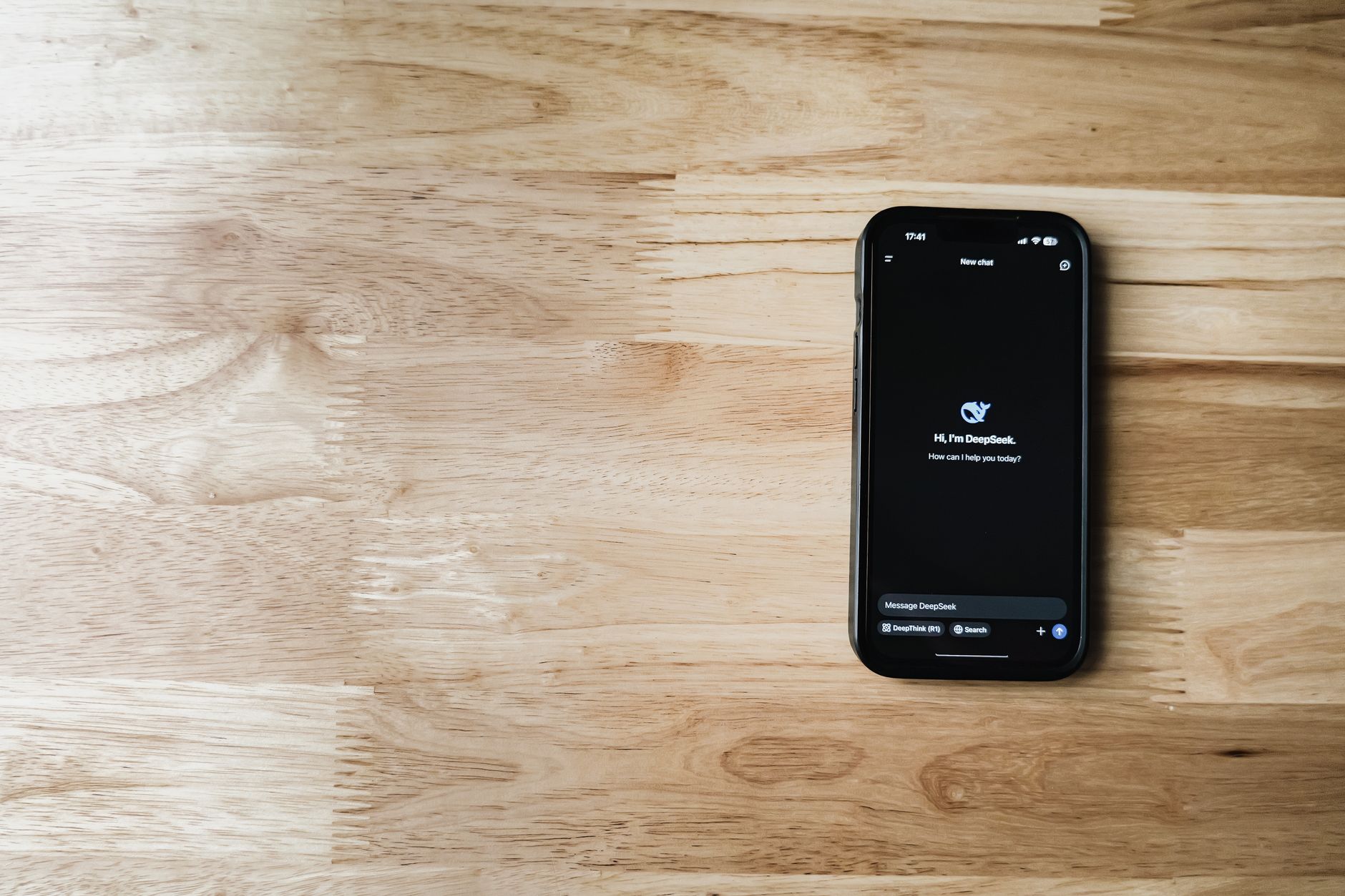 close-up of a smartphone screen displaying a conversational AI language app interface, resting on a wooden desk beside wireless earbuds