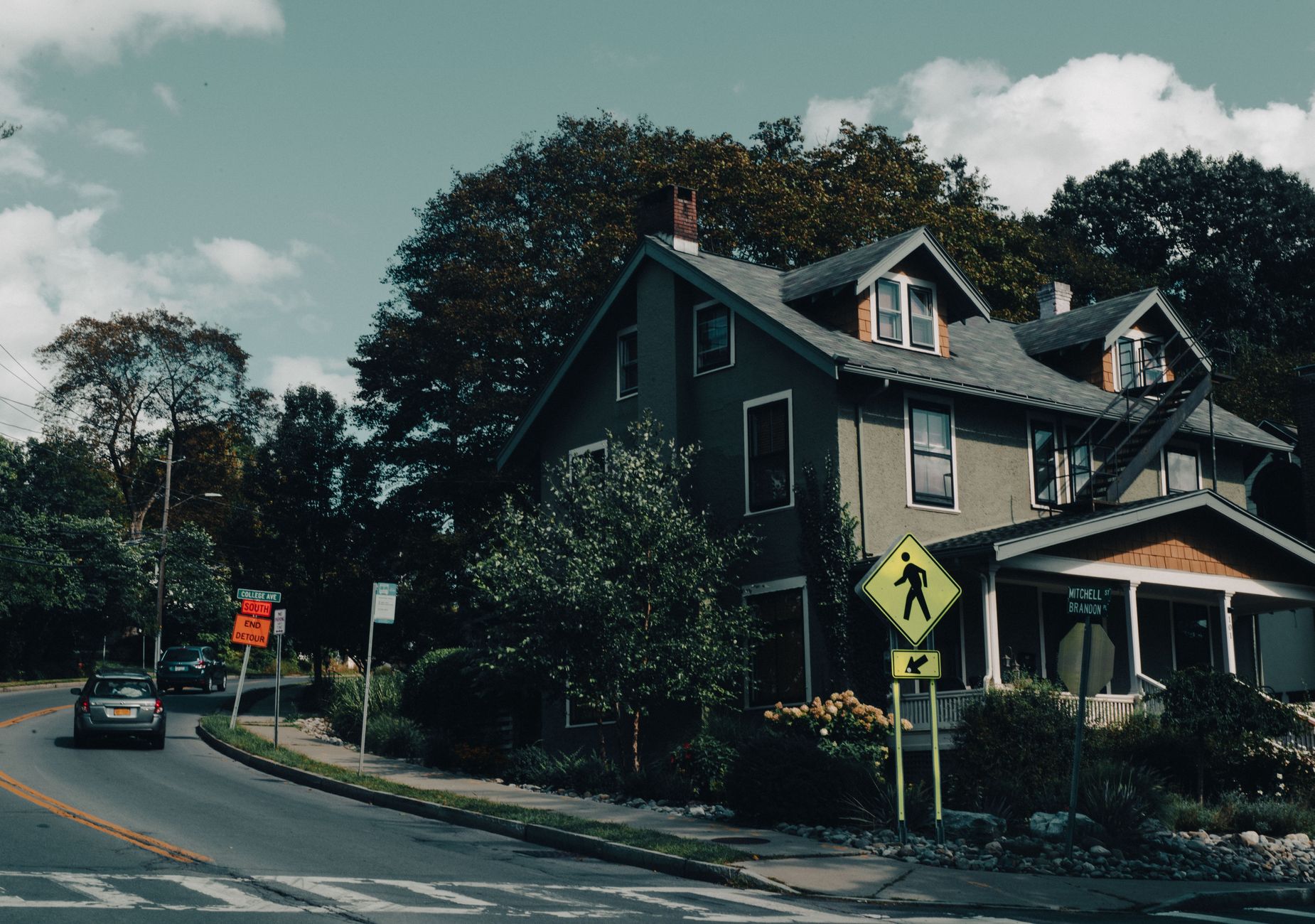 a row of suburban homes with real estate for-sale signs on a quiet residential street in early autumn, leaves just beginning to turn