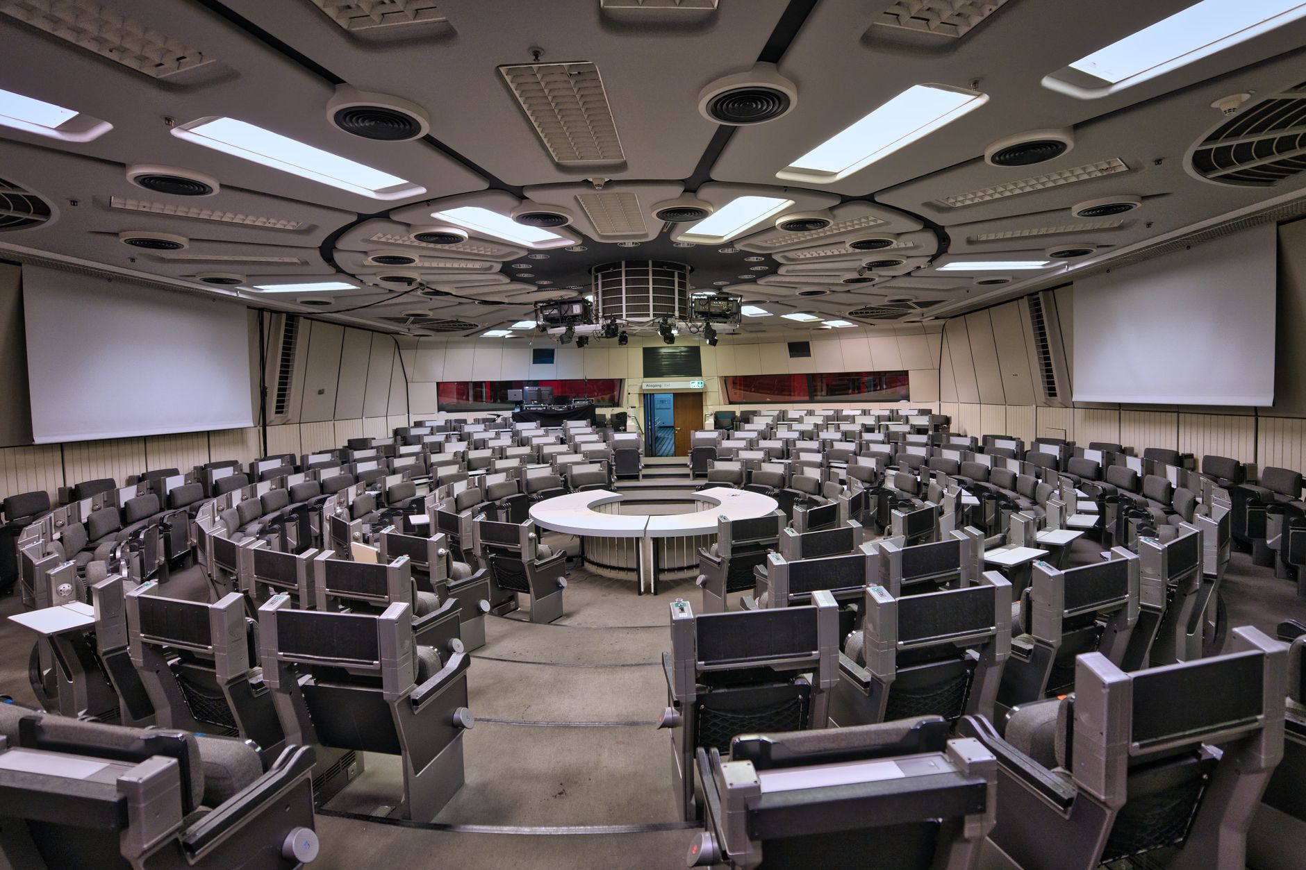 wide interior view of a large modern conference hall with exhibition booths displaying medical technology hardware and digital screens, rows of tables and chairs visible under bright overhead lighting