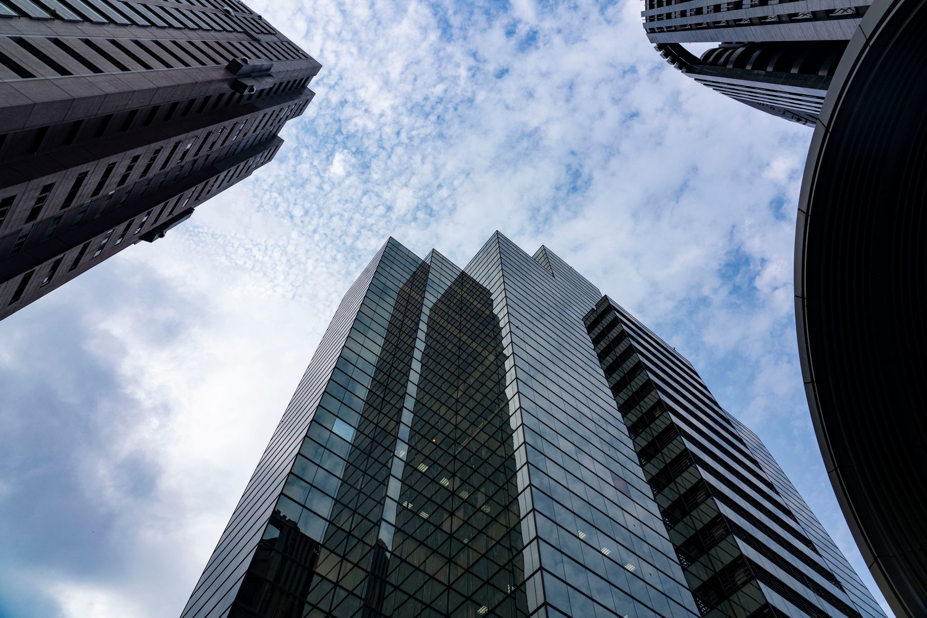 wide-angle view of a corporate campus with glass office towers reflecting a cloudy sky, outdoor plaza empty in early morning light