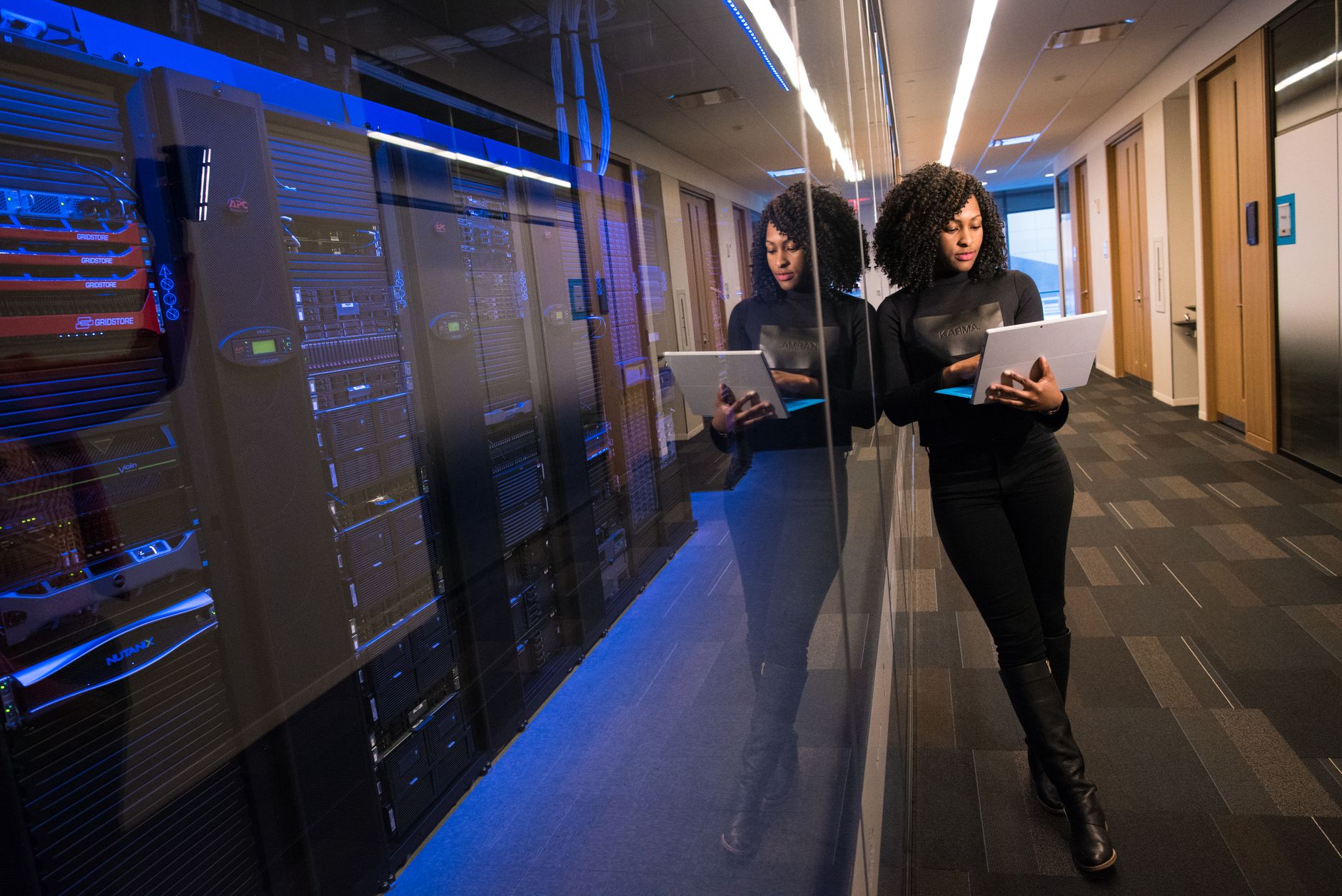 a modern data center corridor lined with server racks illuminated by blue LED lighting, viewed from a low angle looking toward the far end of the aisle