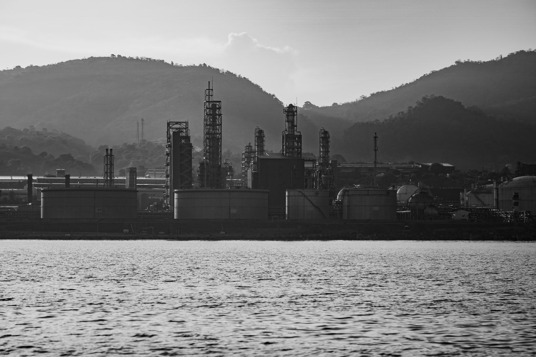 exterior of a large petroleum refinery at dusk with illuminated processing towers reflected in still water