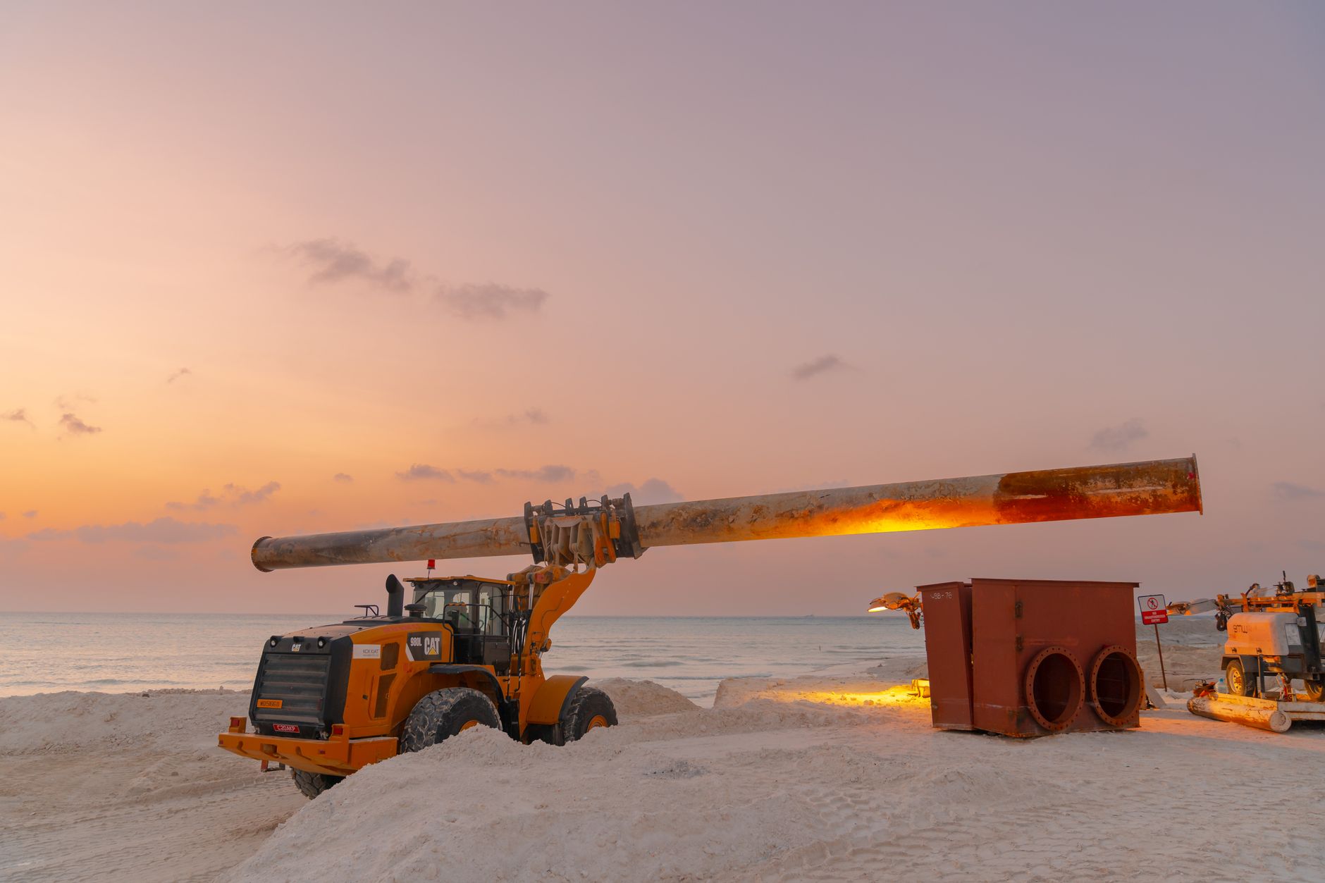 close-up of large-diameter industrial pipeline infrastructure under construction in a flat coastal marshland setting with heavy machinery in the background