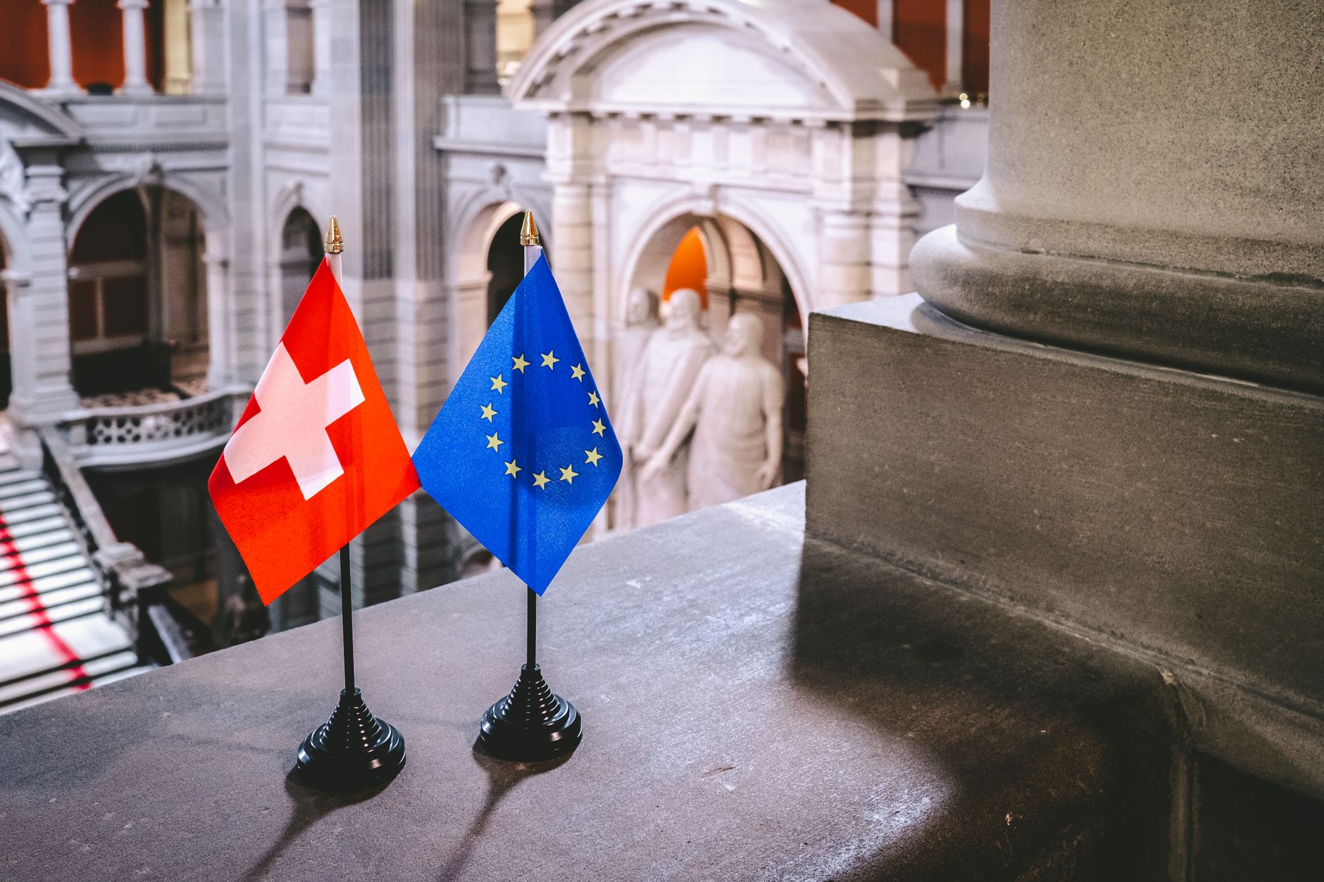 Exterior of a European stock exchange building at dawn, its classical stone facade lit by early morning streetlights with a row of national flags hanging still in calm air