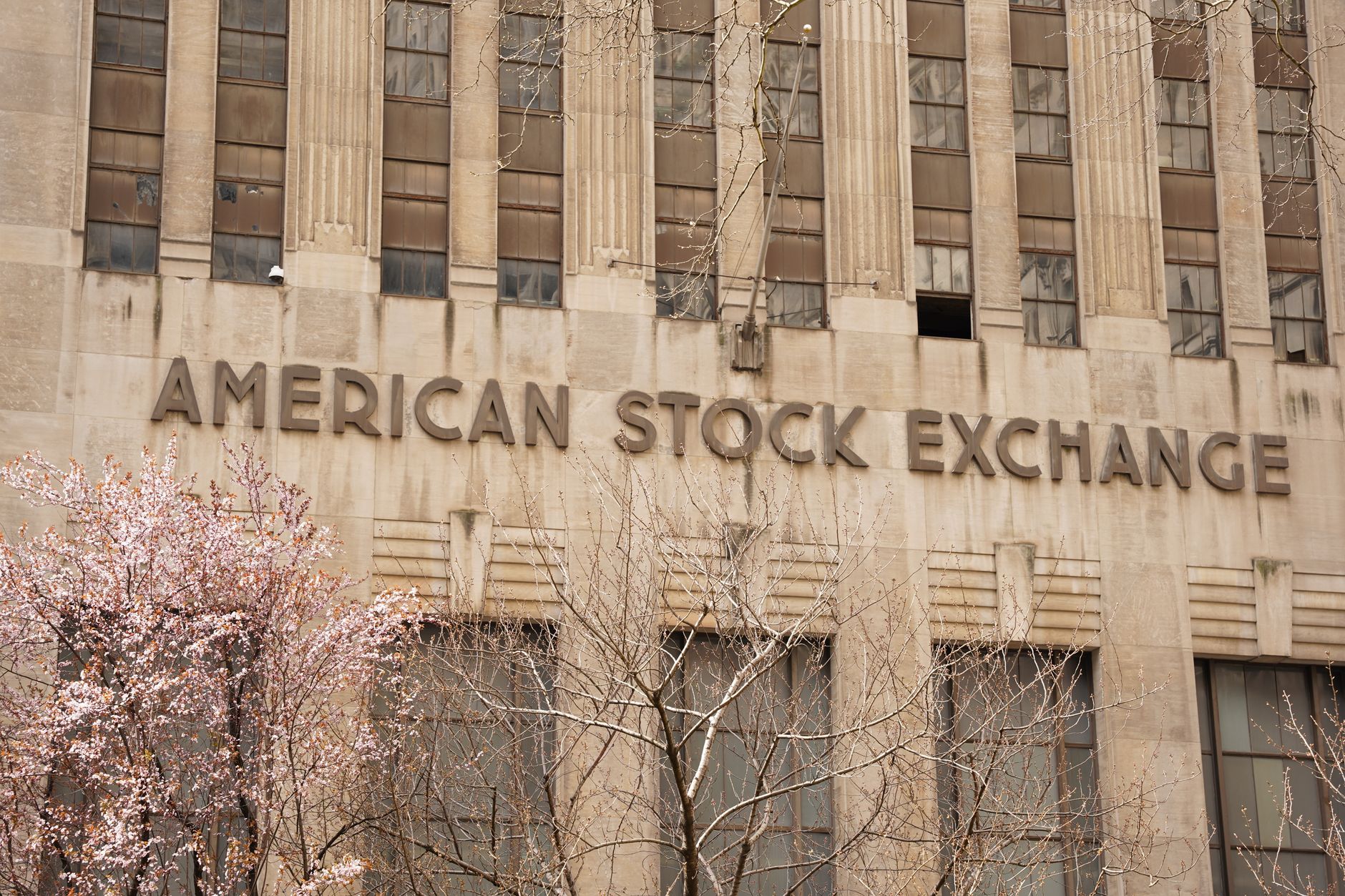 exterior of the New York Stock Exchange building on a clear morning, stone facade and columns visible with flags overhead