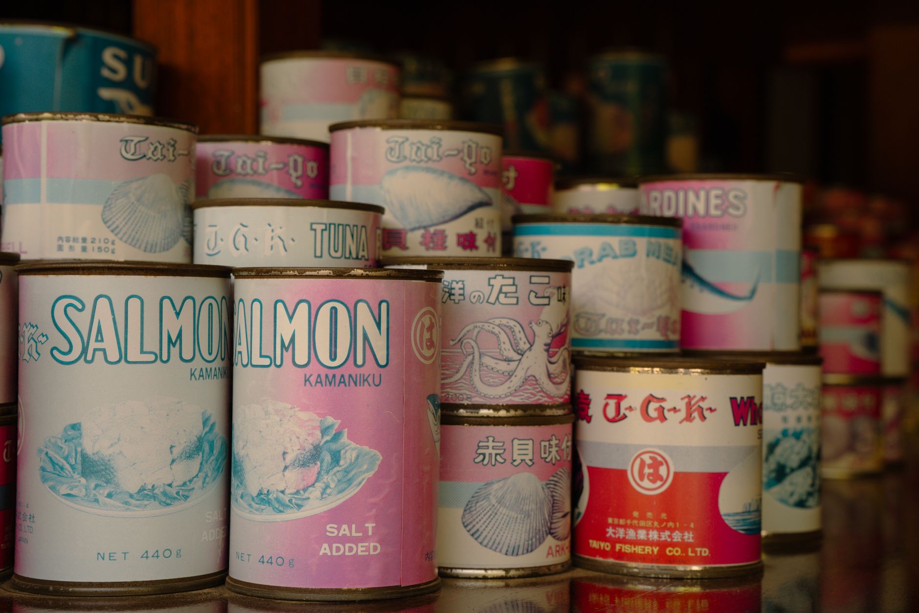 rows of canned fish products on a supermarket shelf, with varying labels and tin sizes visible under fluorescent lighting