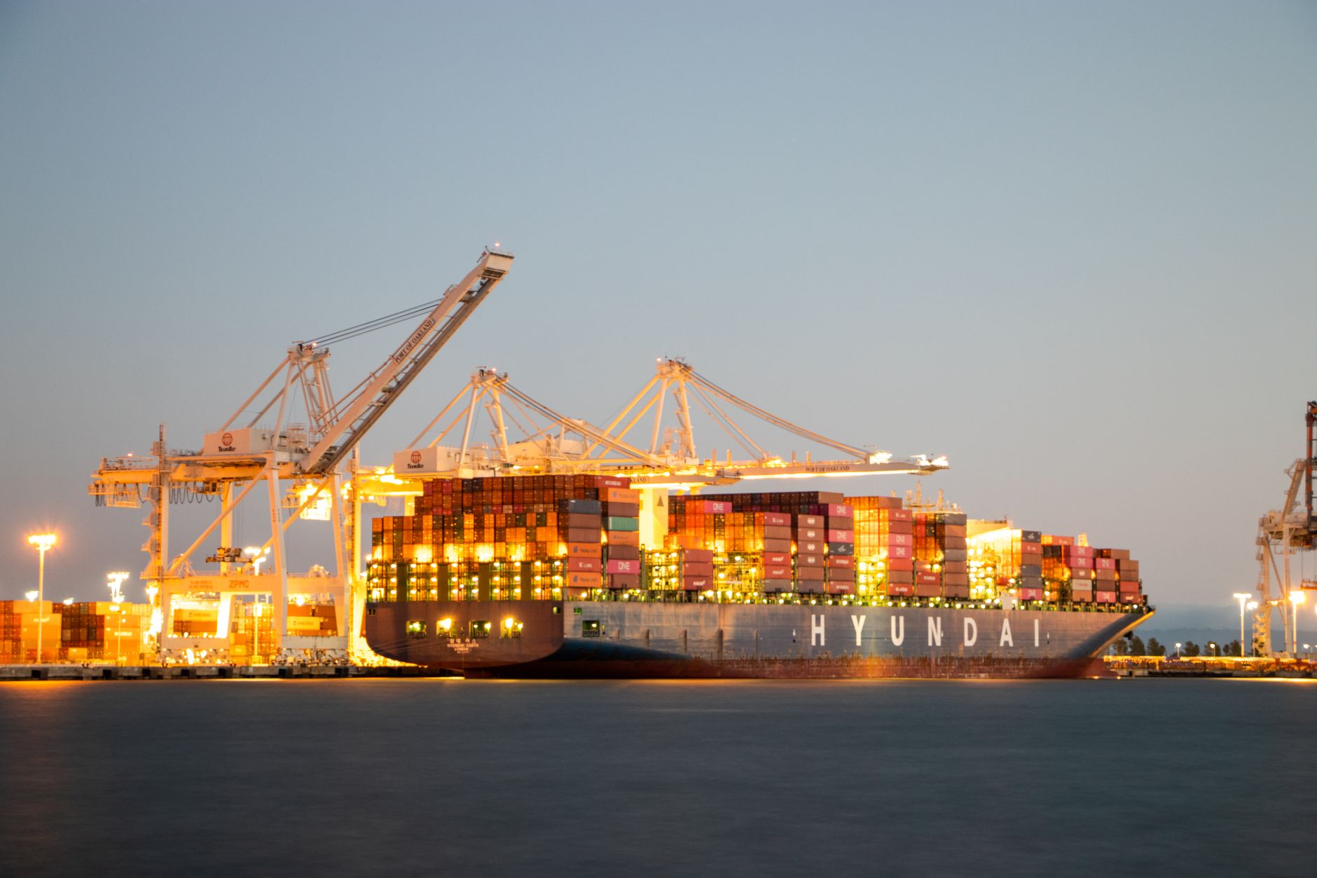 rows of shipping containers stacked at Busan port at dusk, with cargo cranes silhouetted against an orange sky