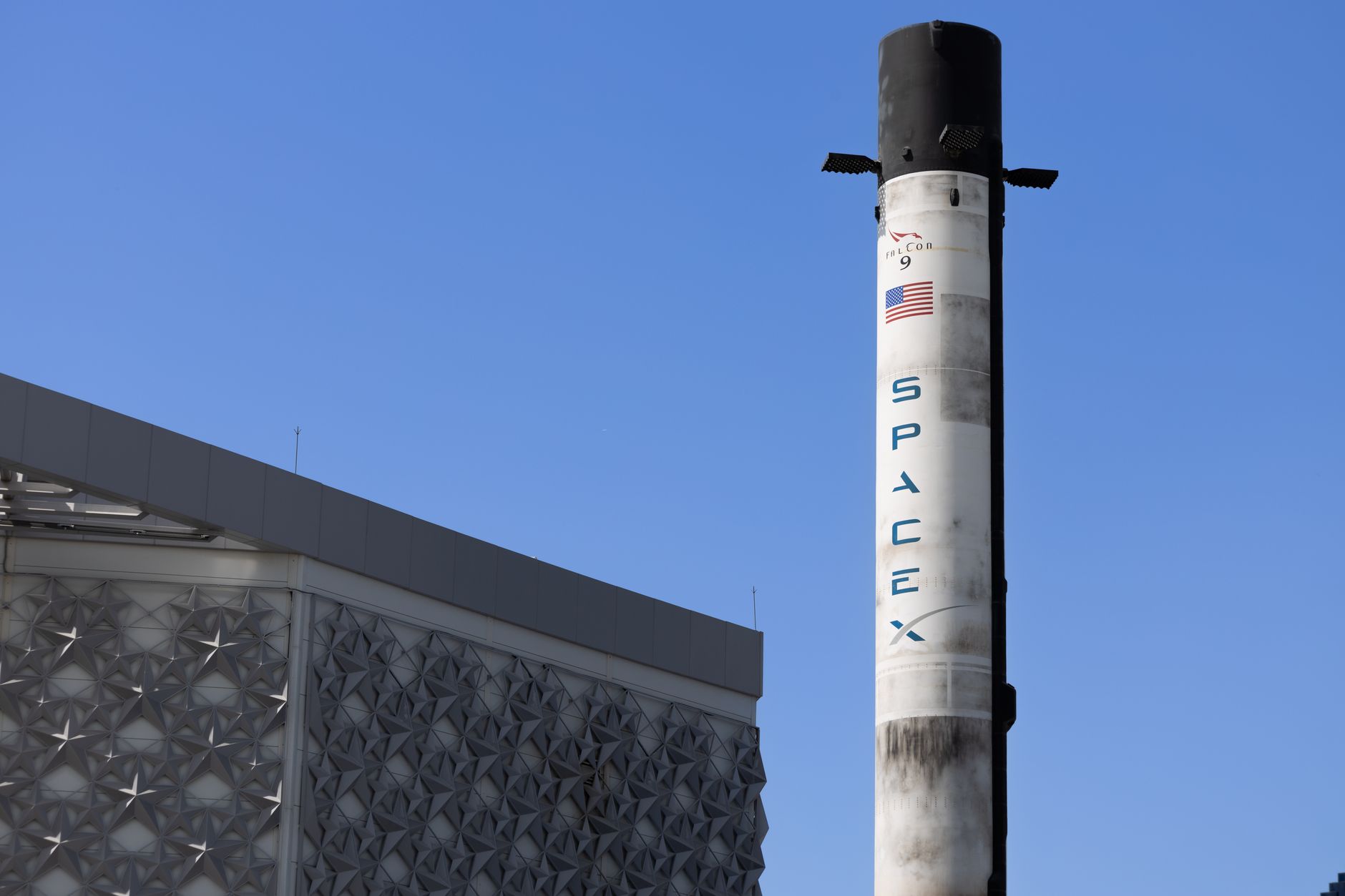 A Falcon 9 rocket standing on a Cape Canaveral launch pad at dusk, surrounded by service structures and floodlights illuminating the launch complex
