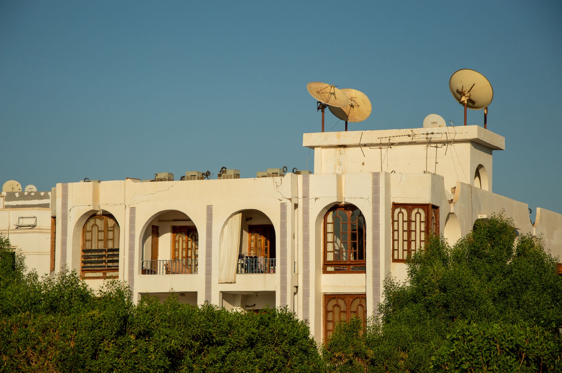 An array of Starlink satellite dishes mounted on the rooftop of a rural residential structure, with open countryside and a clear blue sky in the background