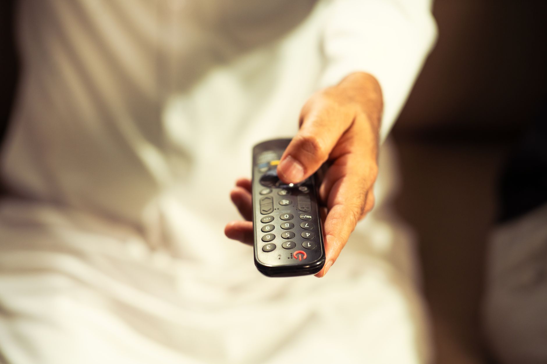a large flat-screen television mounted on a living room wall displaying a grid of streaming channel options, remote control resting on an armrest in the foreground