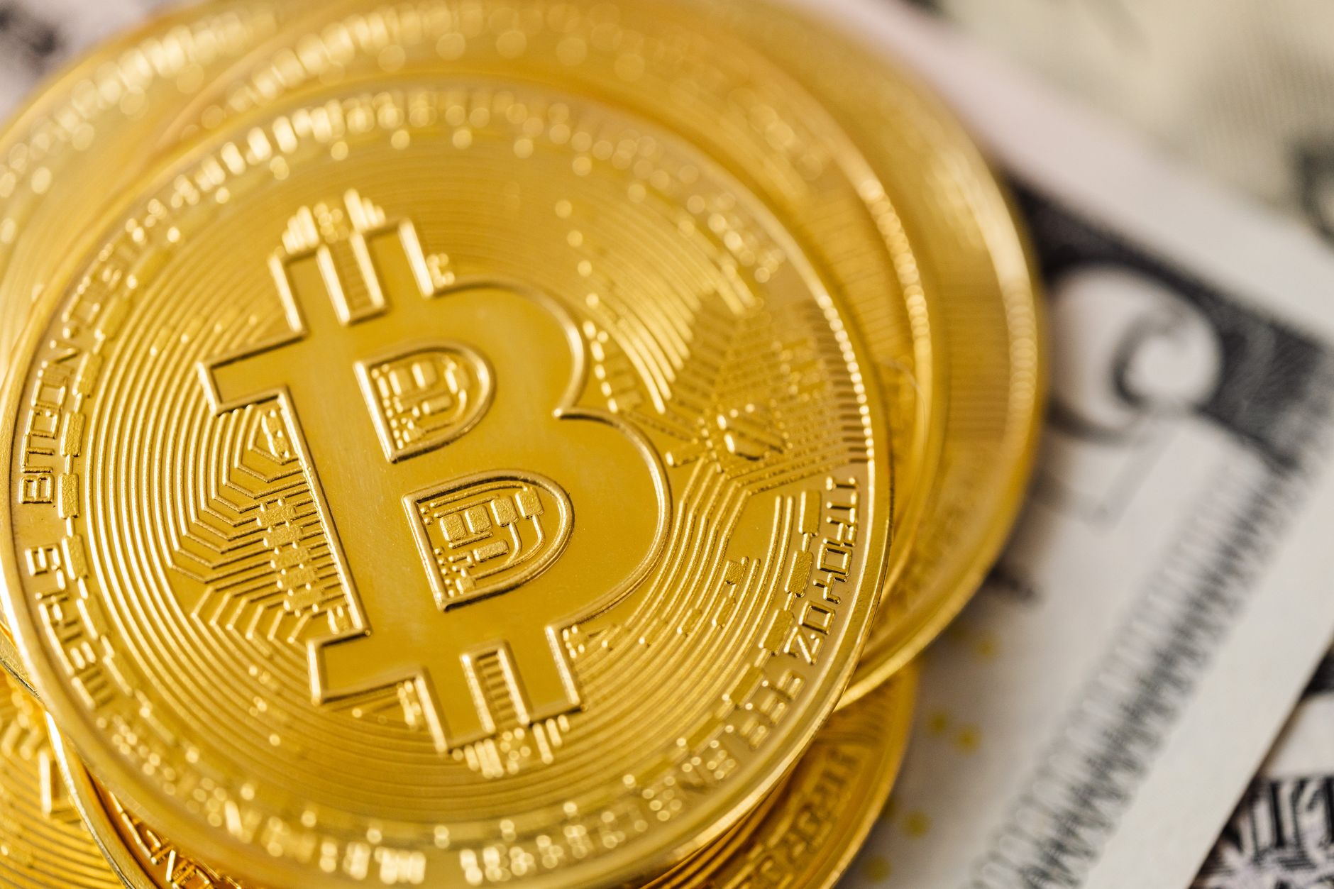 close-up of a physical gold bitcoin token resting on a worn U.S. dollar bill on a wooden desk surface