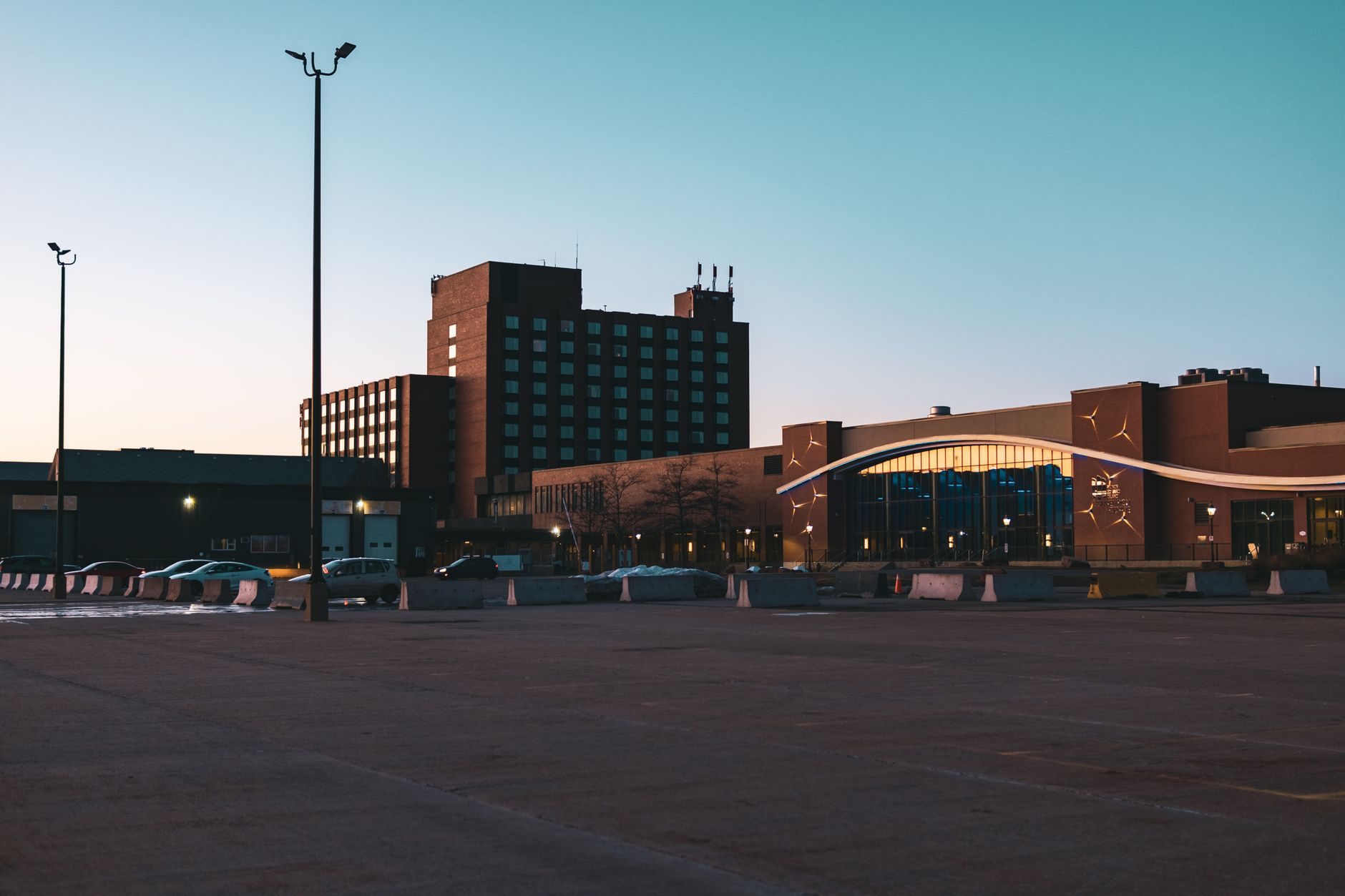 exterior of a mid-sized manufacturing facility at dusk, with a large loading dock and industrial signage visible, parking lot partially empty