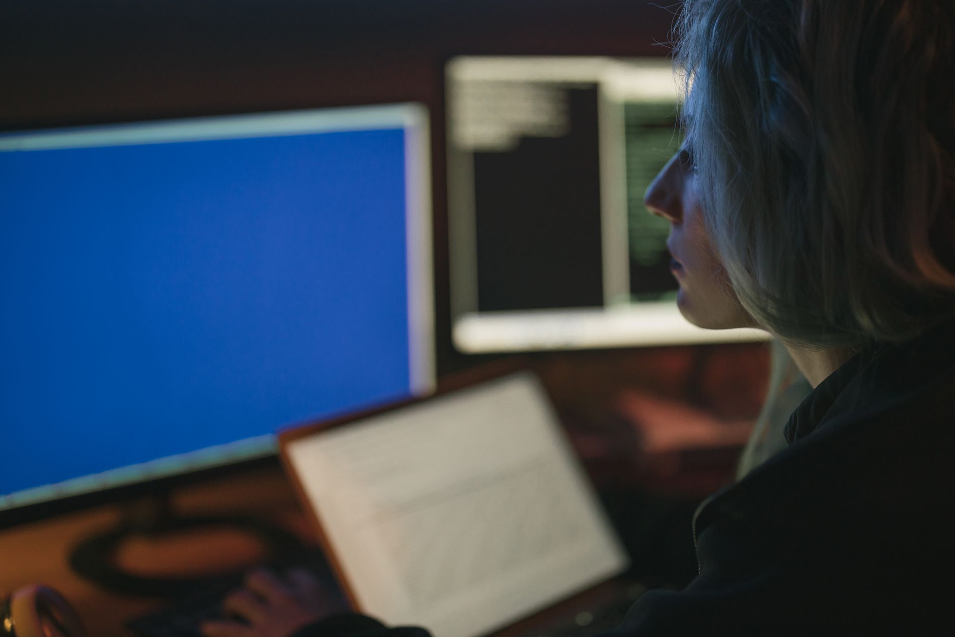 rows of workstations inside a modern AI research laboratory, monitors displaying code and neural network visualisations, ceiling lights casting a cool blue glow over empty chairs late at night