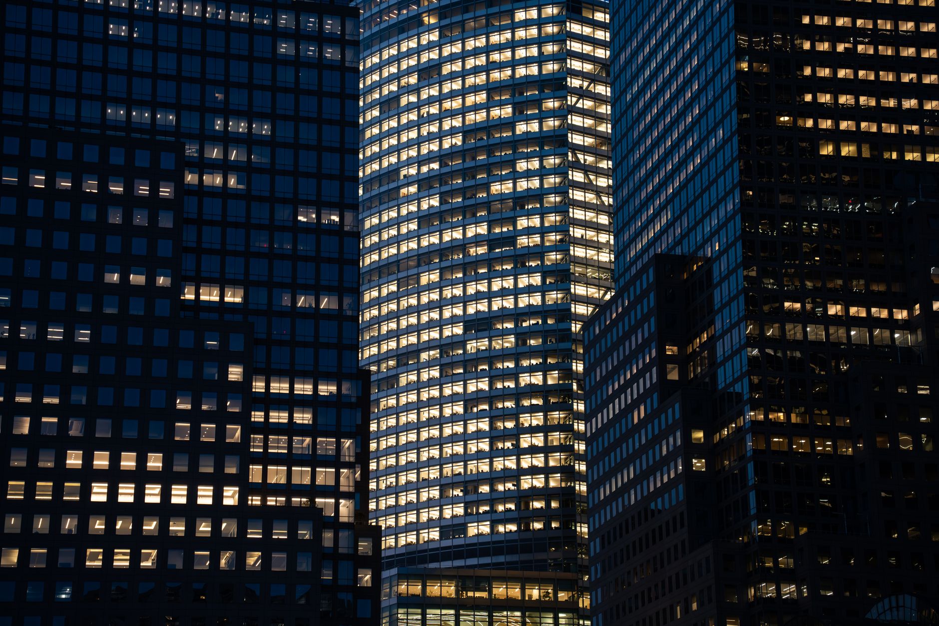 a modern customer experience operations centre at night, rows of illuminated workstations visible through floor-to-ceiling glass walls in an urban high-rise setting