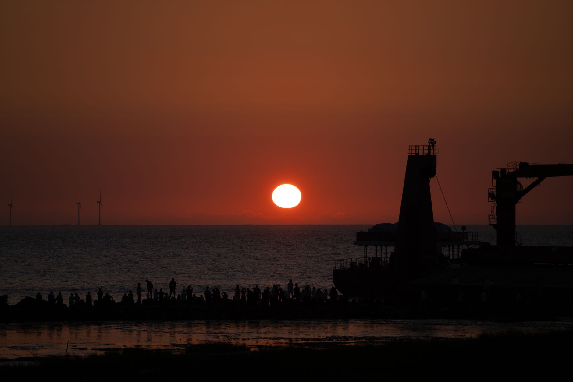 aerial view of an offshore oil platform in the Persian Gulf at dusk, industrial flare burning against an orange sky