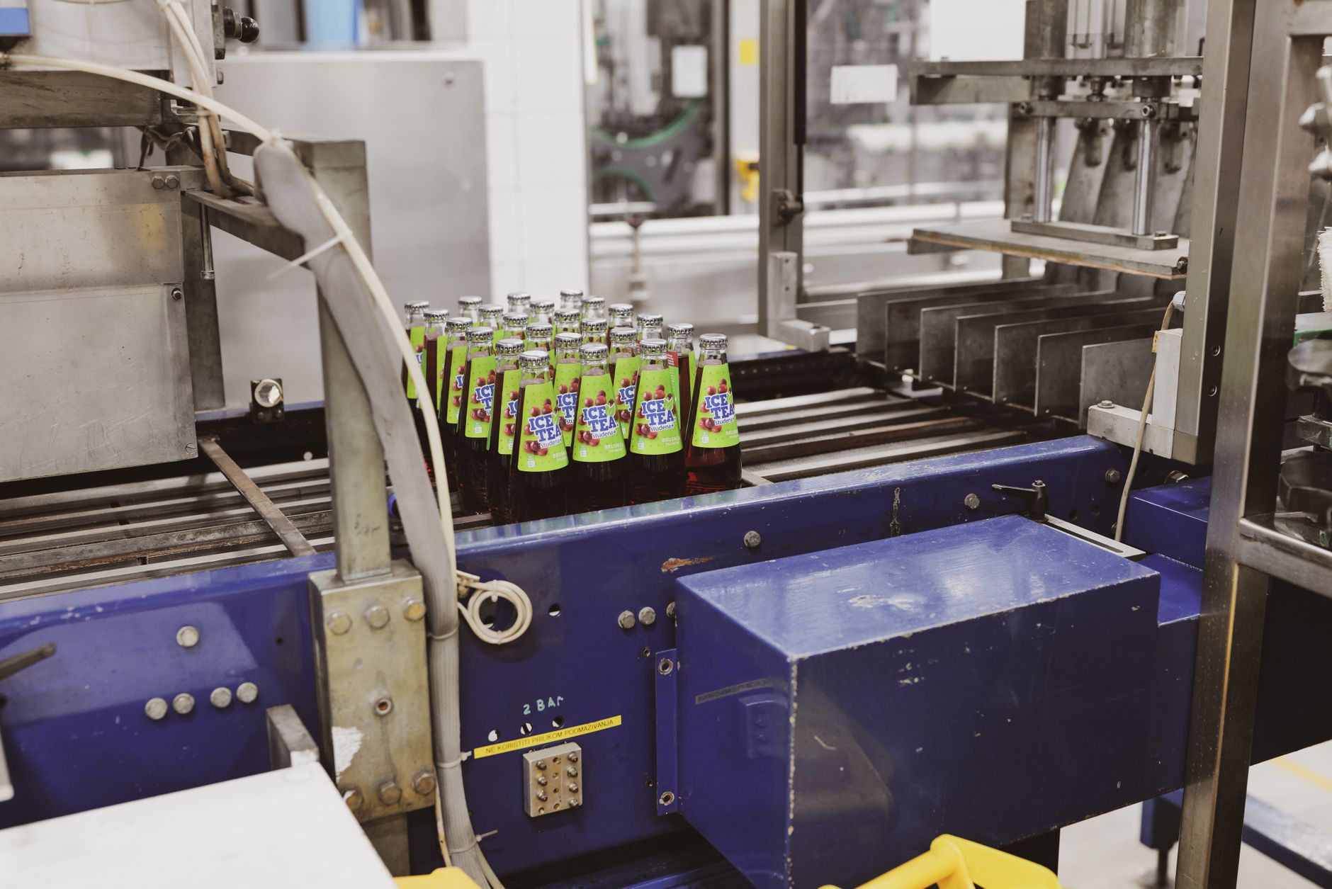 rows of product packaging on a factory conveyor belt inside a large automated consumer goods plant, with machinery and ceiling-mounted lighting visible