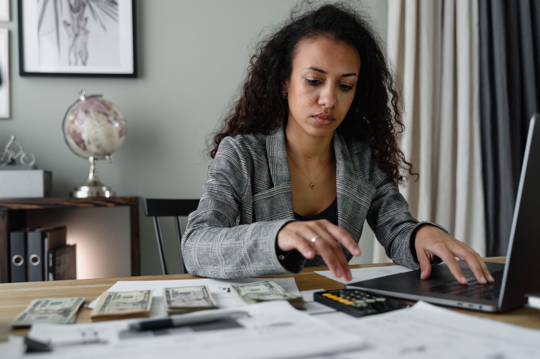 a modest apartment kitchen counter with an open laptop showing a brokerage account interface, scattered bills and a notepad nearby