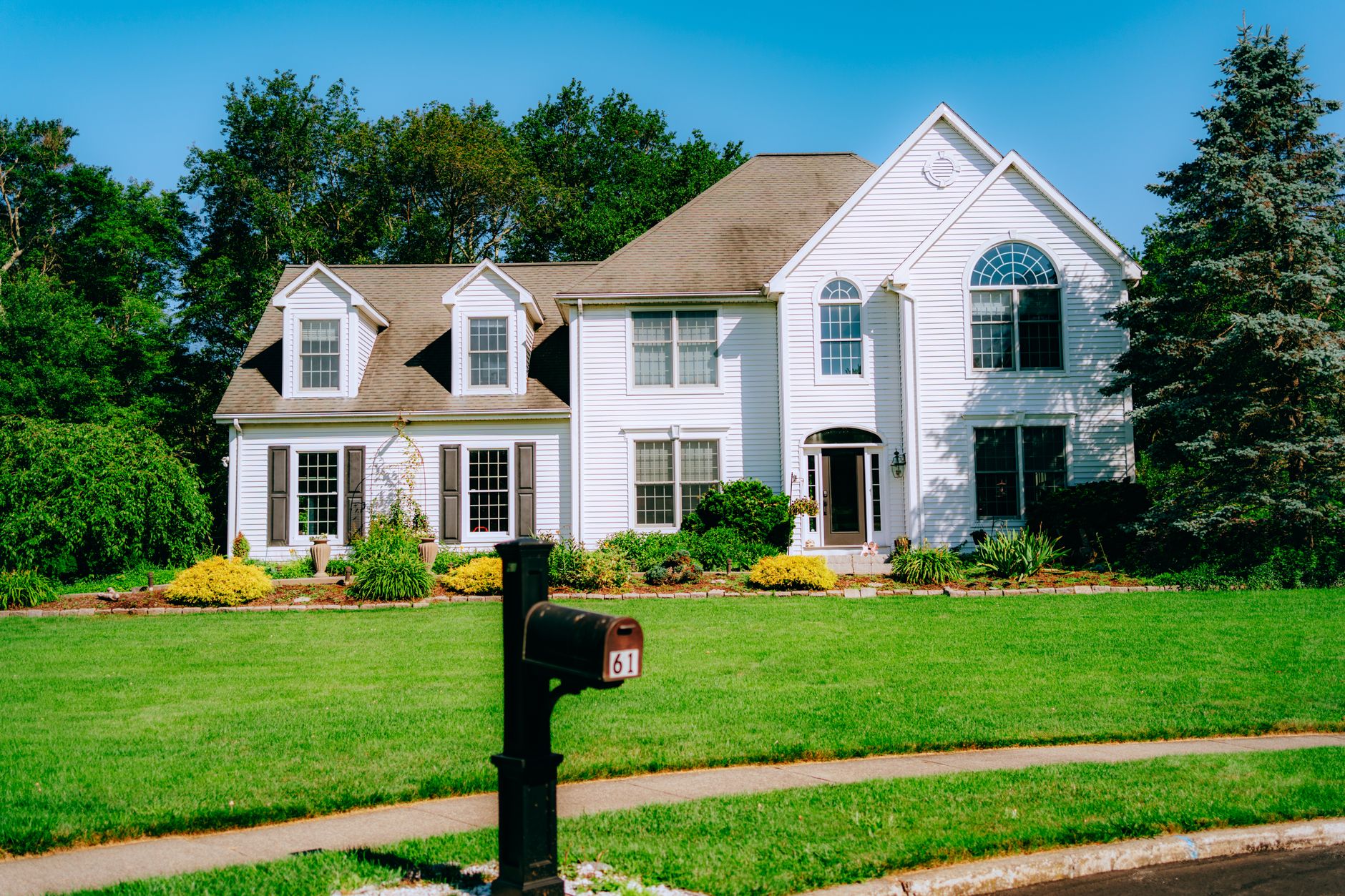 a suburban home exterior with a visible mailbox and a mowed front lawn on a quiet street, representing middle-class family wealth and property