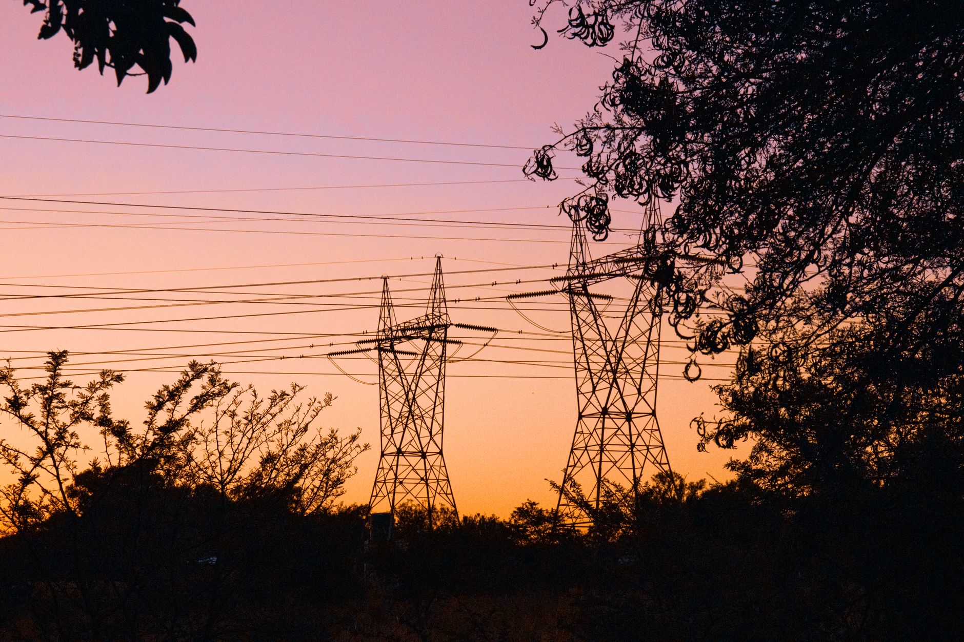 close-up of an industrial electricity pylon at dusk with transmission lines stretching into a hazy orange sky