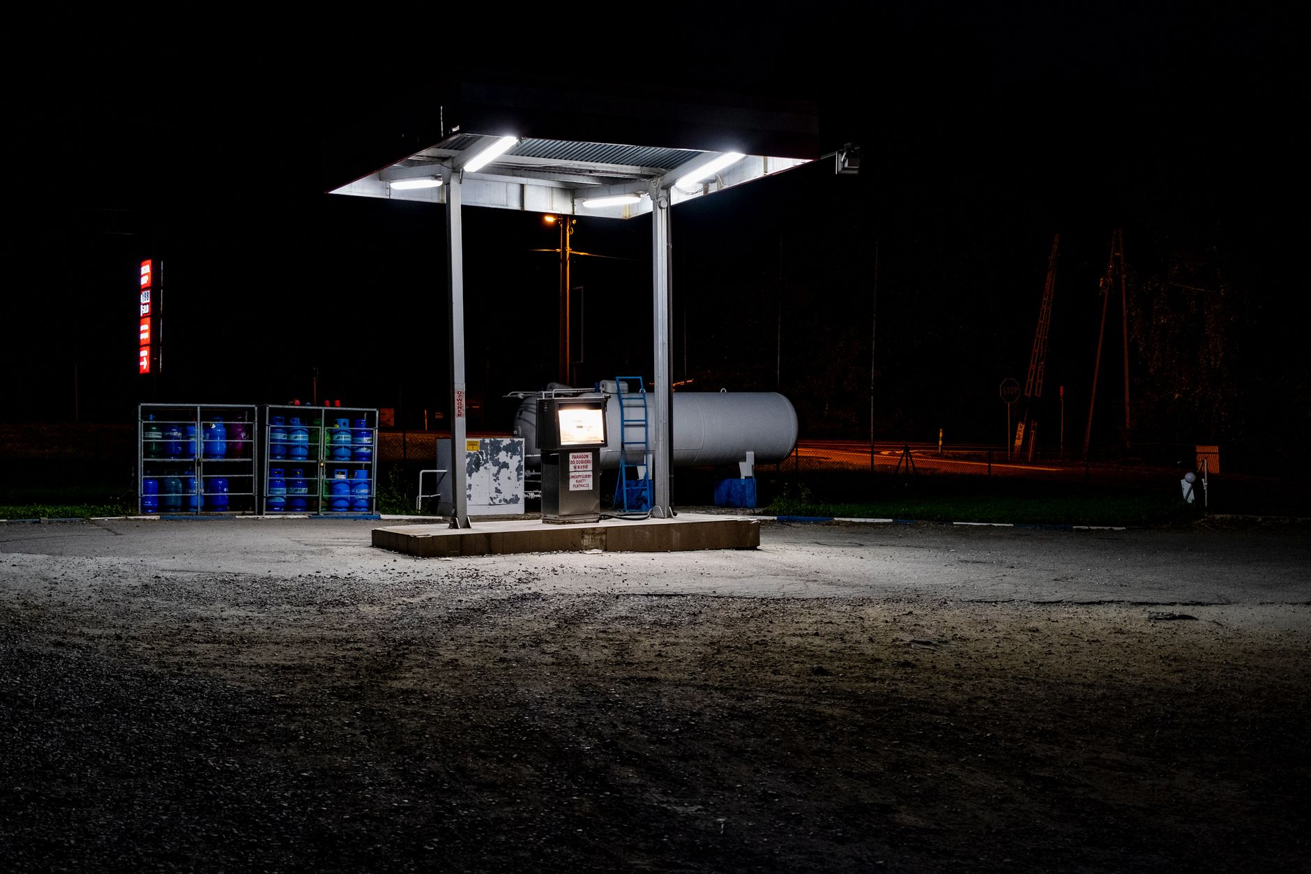exterior of a petrol station forecourt at night with illuminated price display boards showing elevated fuel costs