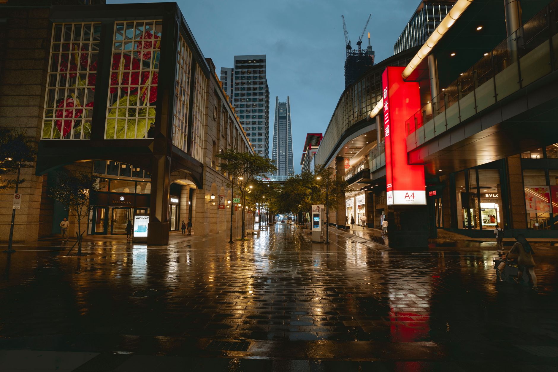 exterior of a modern financial district building at dusk with illuminated windows reflected in wet pavement, no people as the focal point