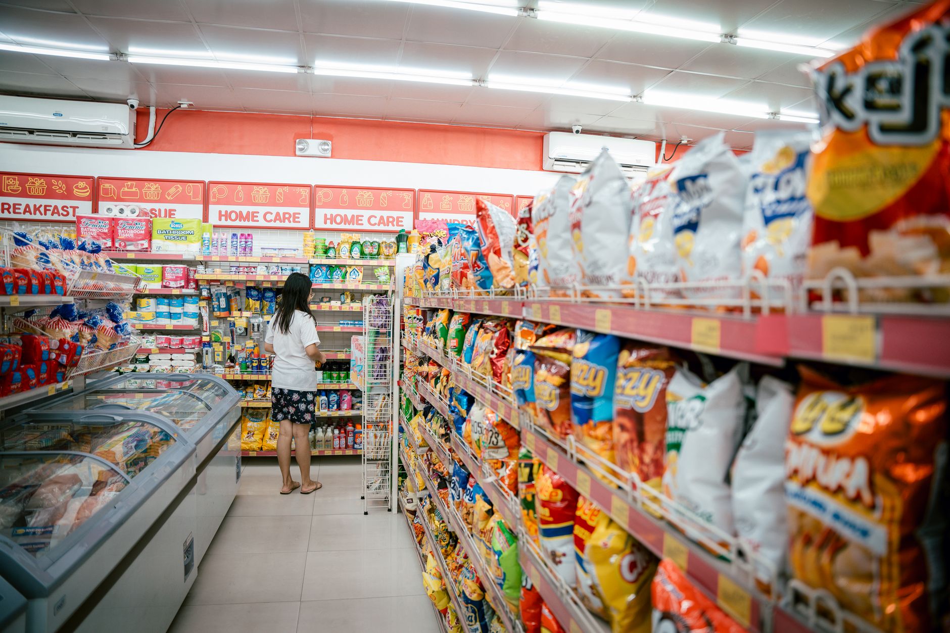 a grocery store aisle with shelves stocked with packaged goods and handwritten price tags visible on the edge of the shelving units