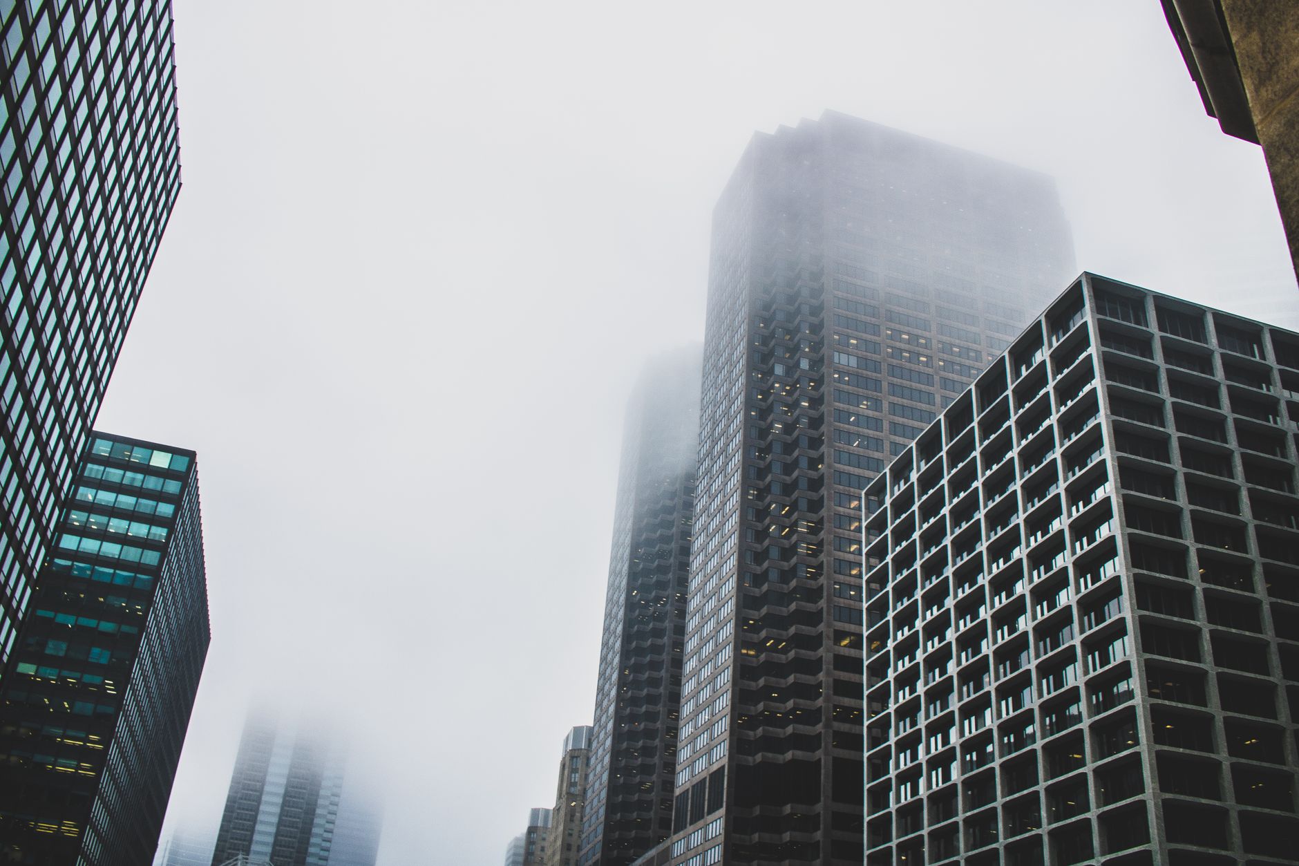 wide exterior shot of a glass-fronted corporate office tower in a downtown financial district on an overcast morning, with sparse street-level activity visible below