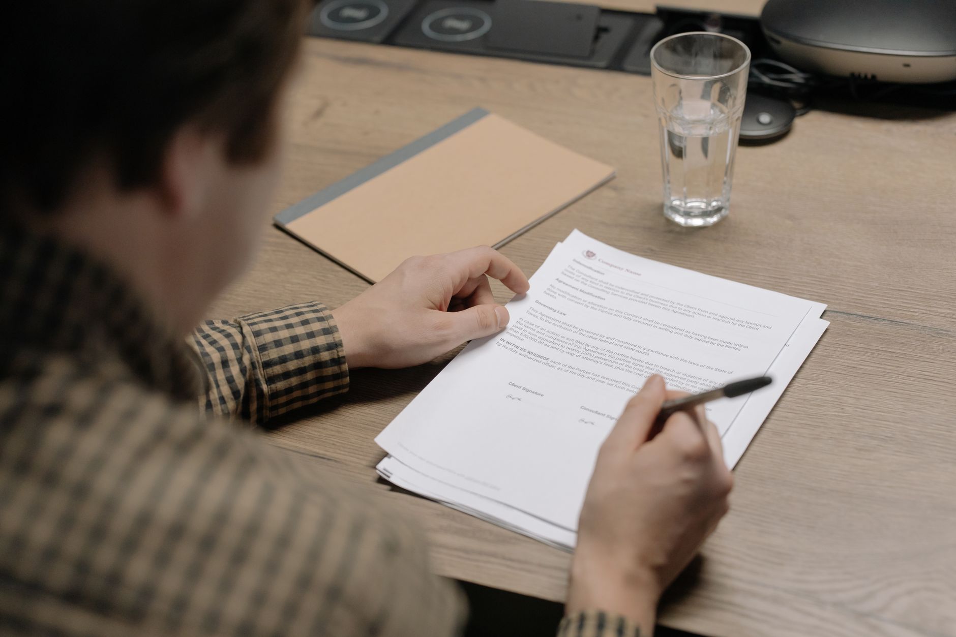 a signed legal document resting on a wooden desk beside a set of house keys and a ballpoint pen, natural window light falling across the page