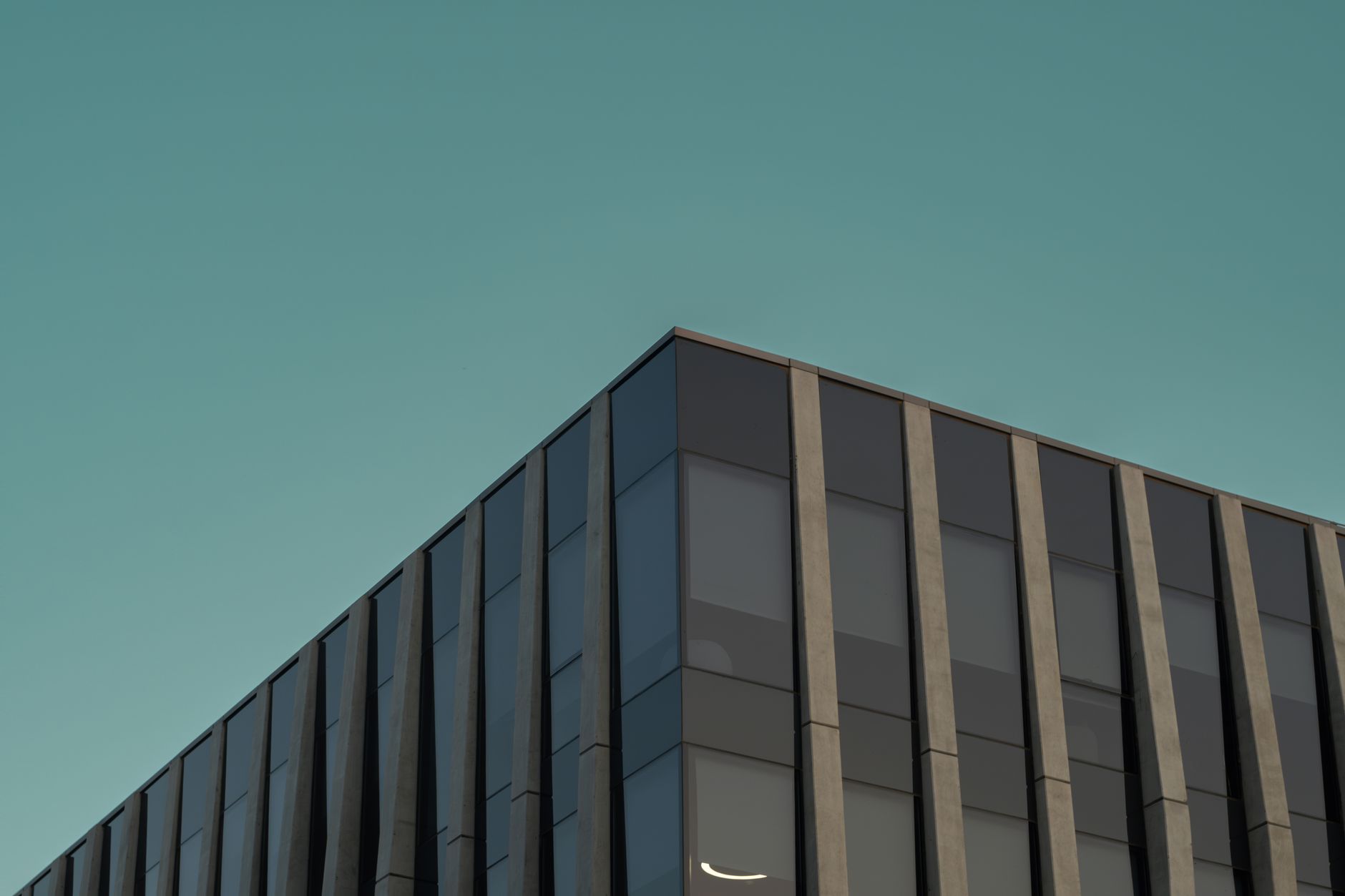 exterior of a modern corporate office building with glass facade reflecting afternoon light, set against a clear blue sky