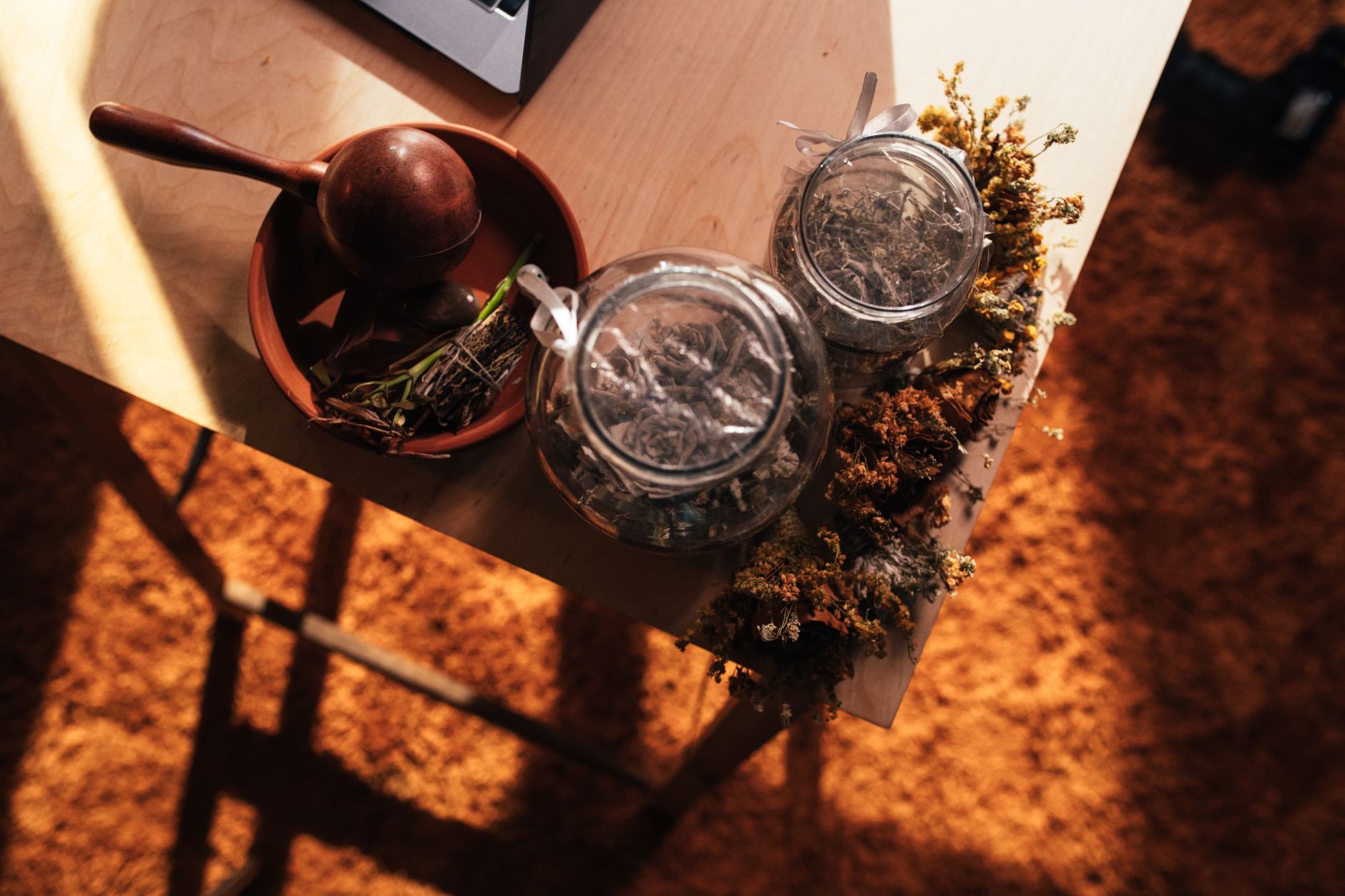 close-up of dried medicinal plant roots and leaves arranged on a wooden surface in a traditional Ayurvedic dispensary, with ceramic jars in the background