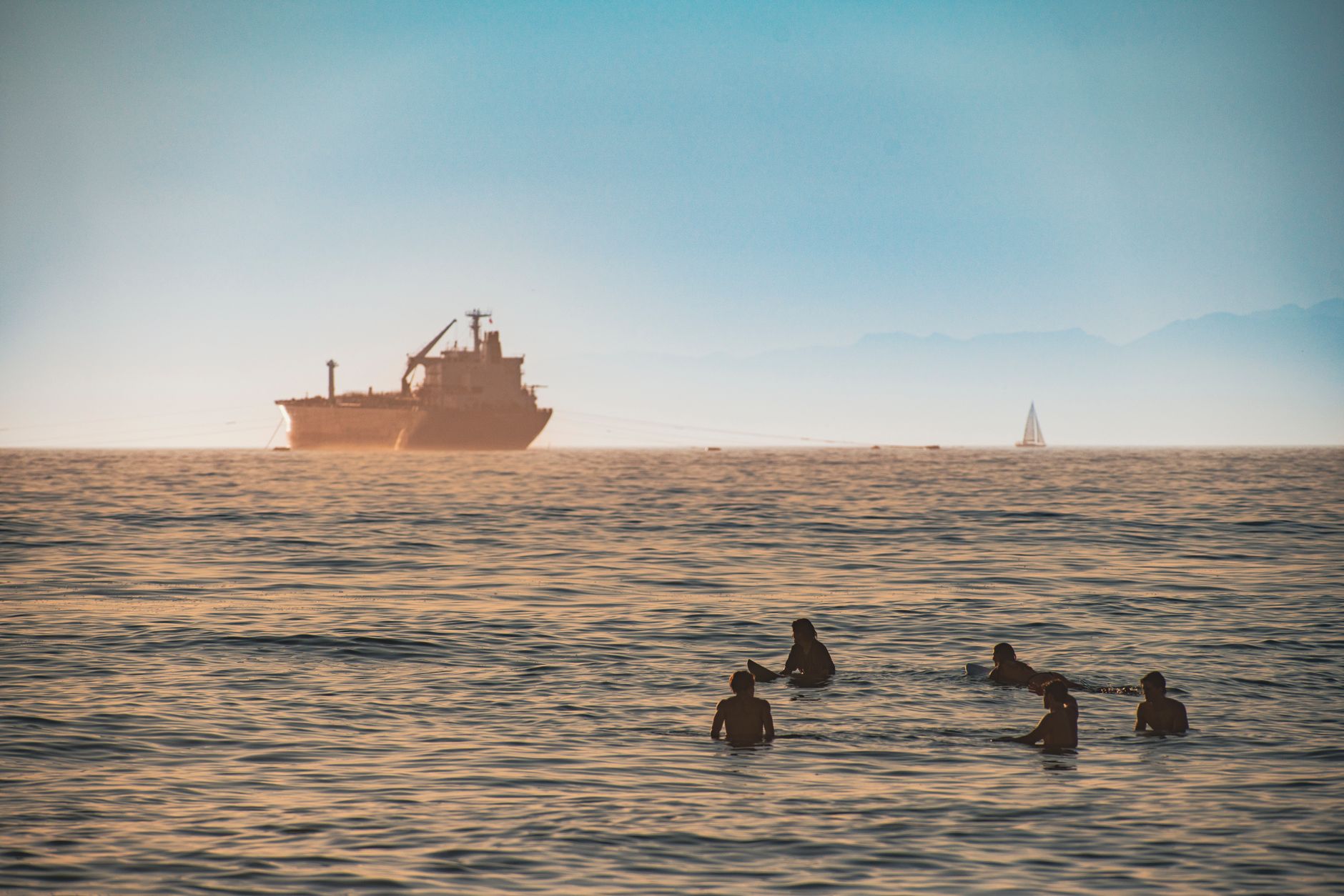 aerial view of oil tankers anchored in open water near a strait, surrounded by a hazy industrial haze at dusk