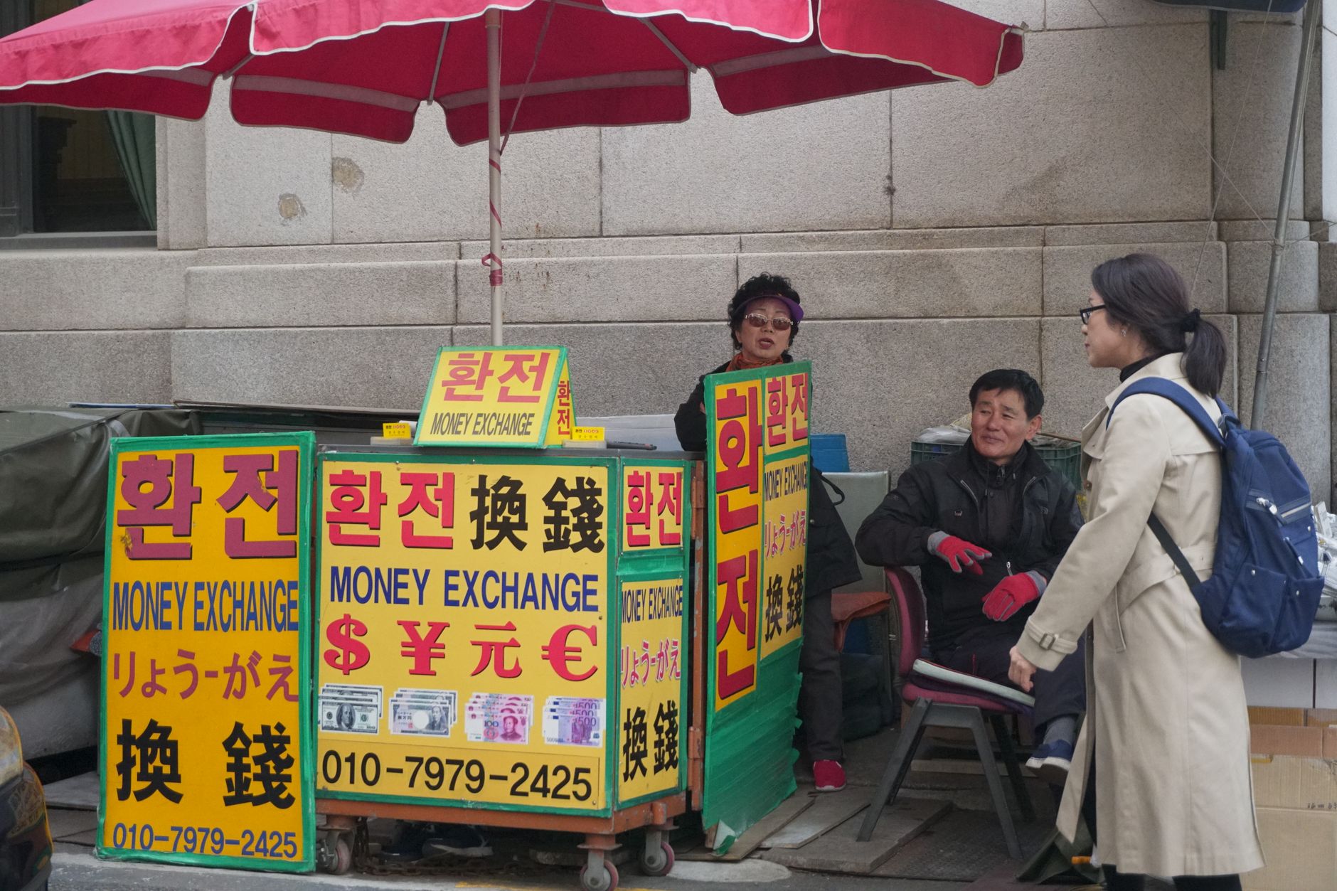 currency exchange booth exterior in a busy urban street with worn signage displaying dollar and euro rates
