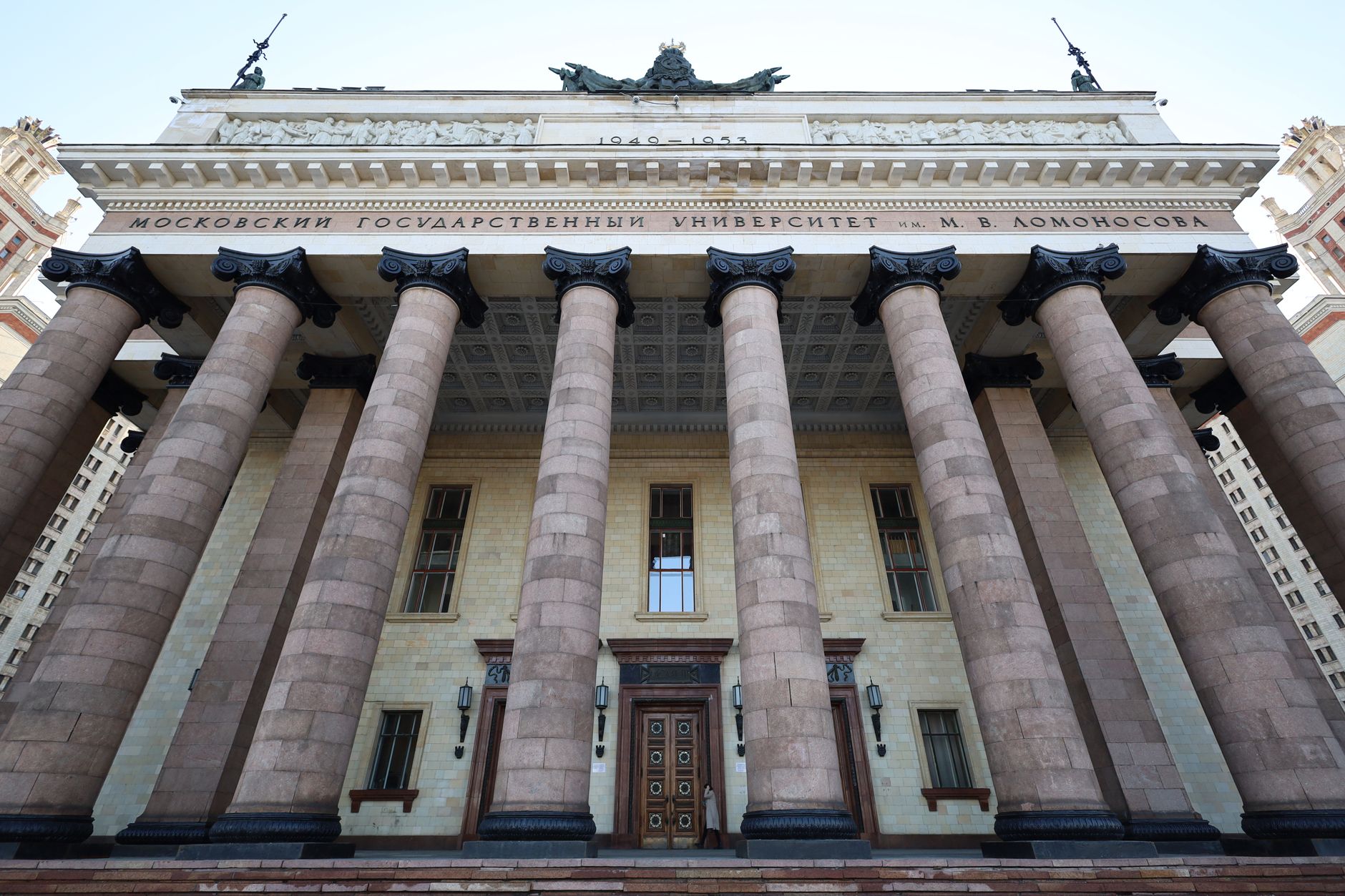 wide-angle view of a U.S. government building entrance with stone columns and brass signage, early morning light on the facade