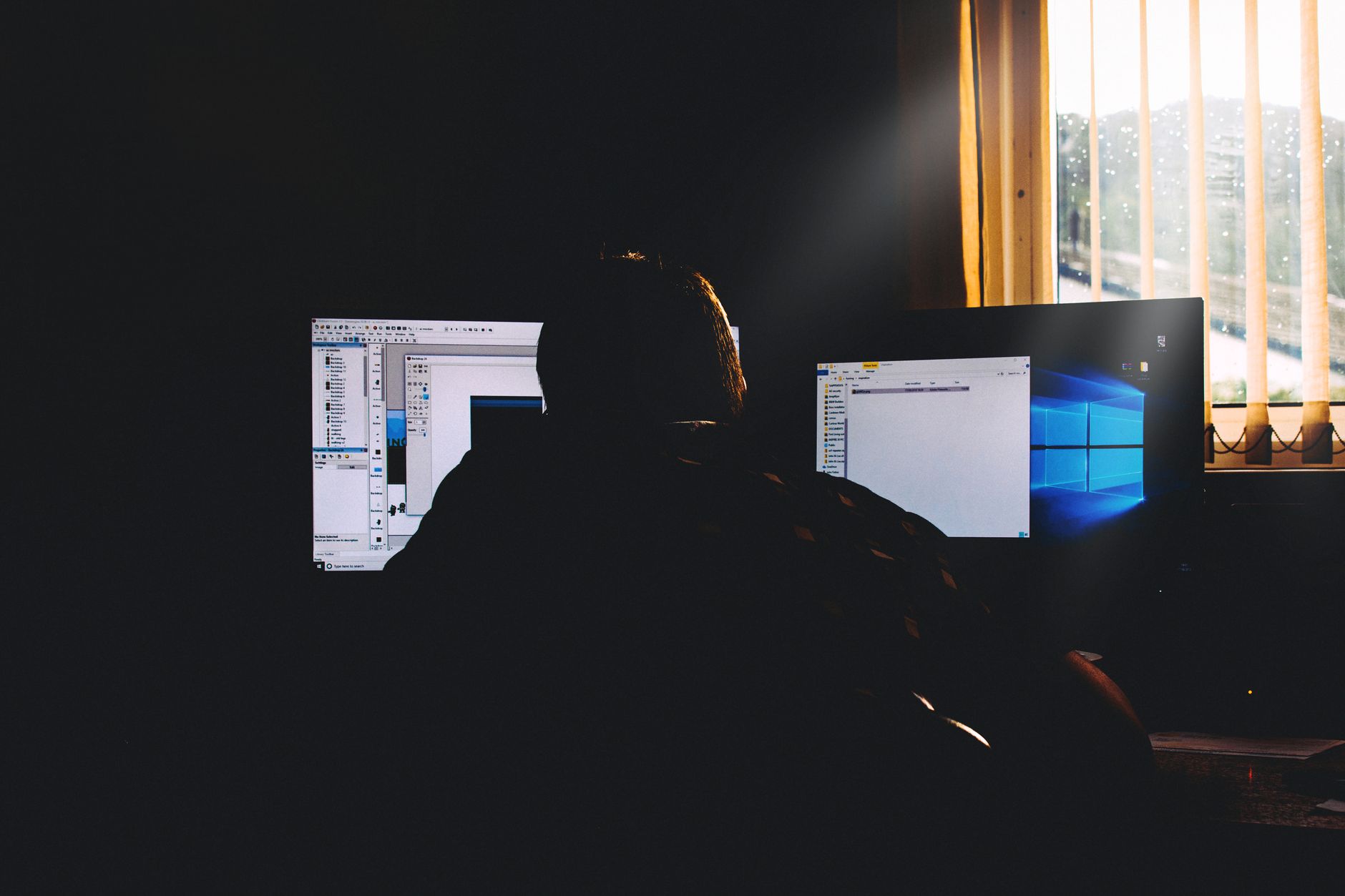 rows of empty desks and monitors in a dimly lit open-plan technology office, chairs pushed in