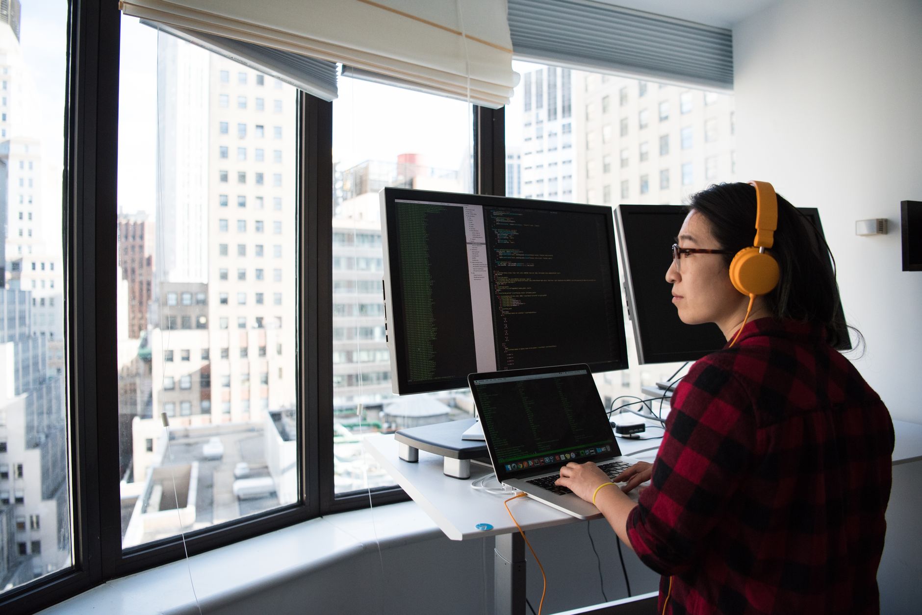 interior of a modern software development office, rows of empty standing desks with monitors powered down, natural light from floor-to-ceiling windows
