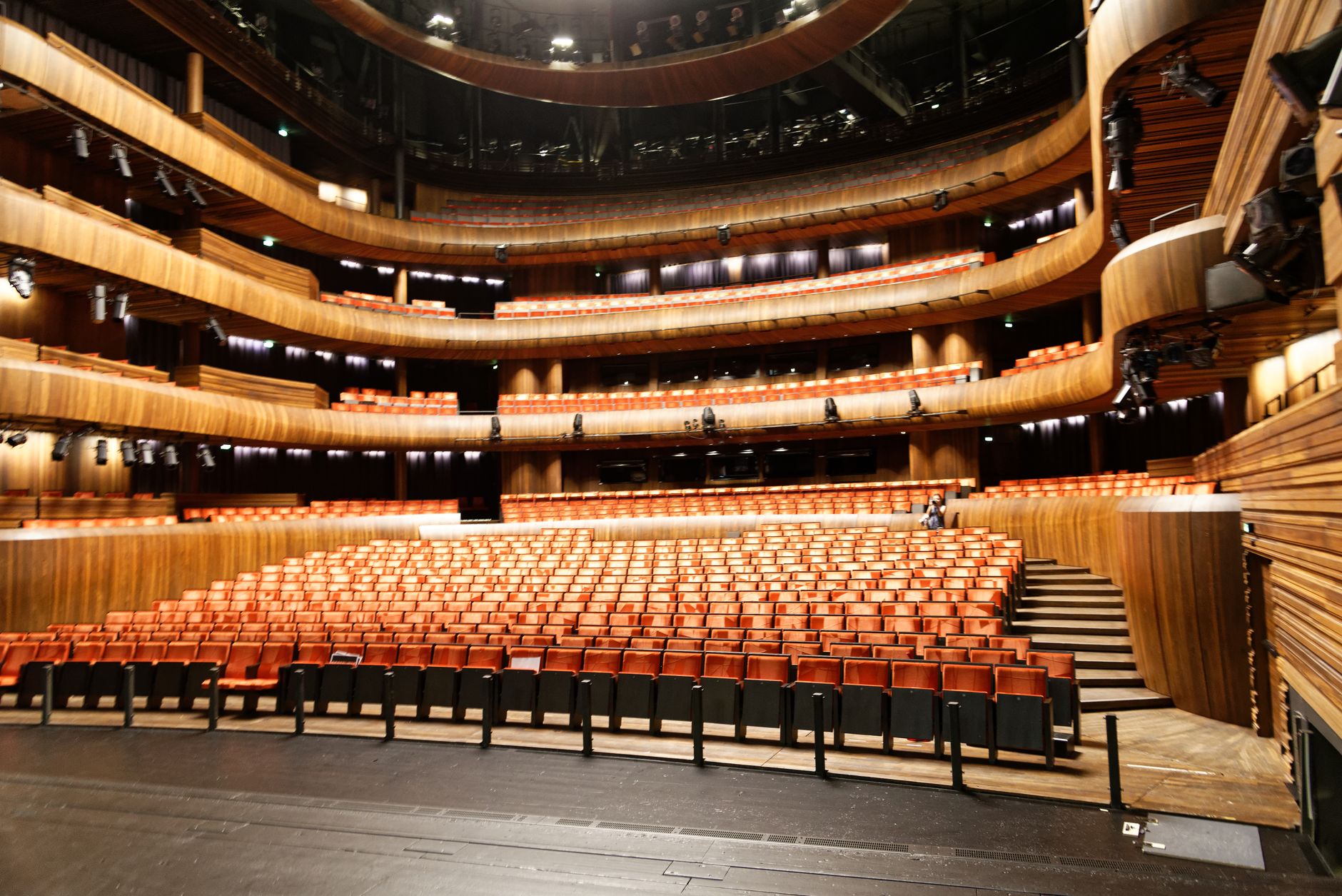 wide-angle exterior of a mid-sized American arena venue at dusk, with rows of empty folding chairs visible through open doors and campaign signage being arranged on a stage in the background