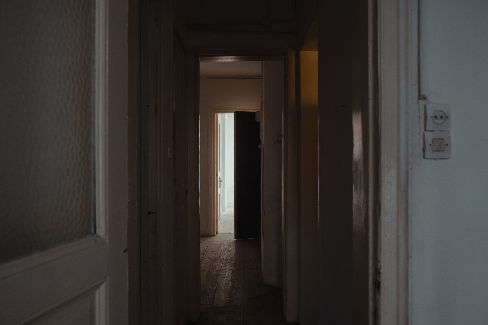 long corridor inside a congressional office building with marble floors, rows of closed wooden doors, and overhead fluorescent lighting casting a formal, institutional atmosphere