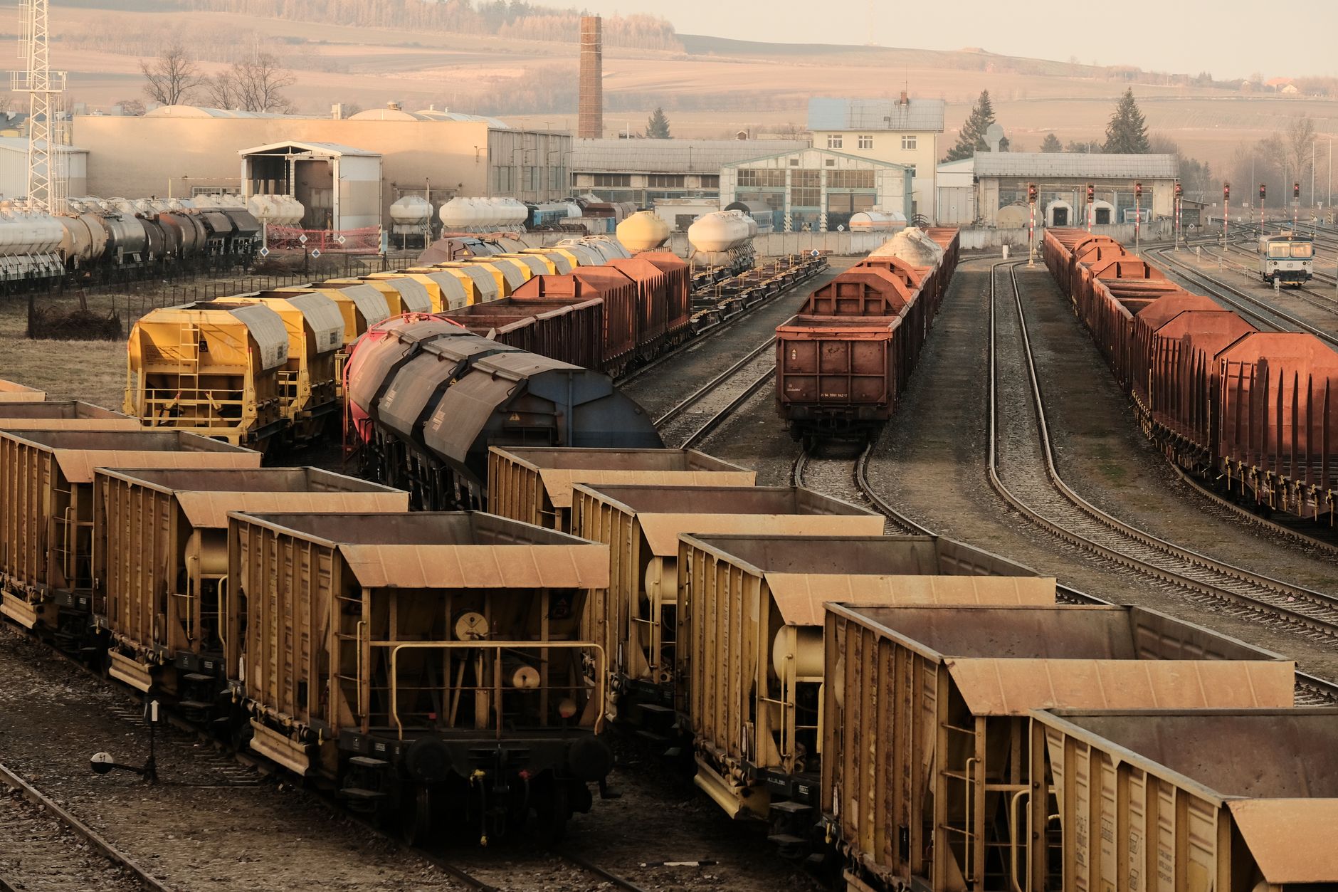 a freight locomotive undergoing maintenance inside a large industrial rail depot, with overhead lighting illuminating steel components and repair equipment on the workshop floor